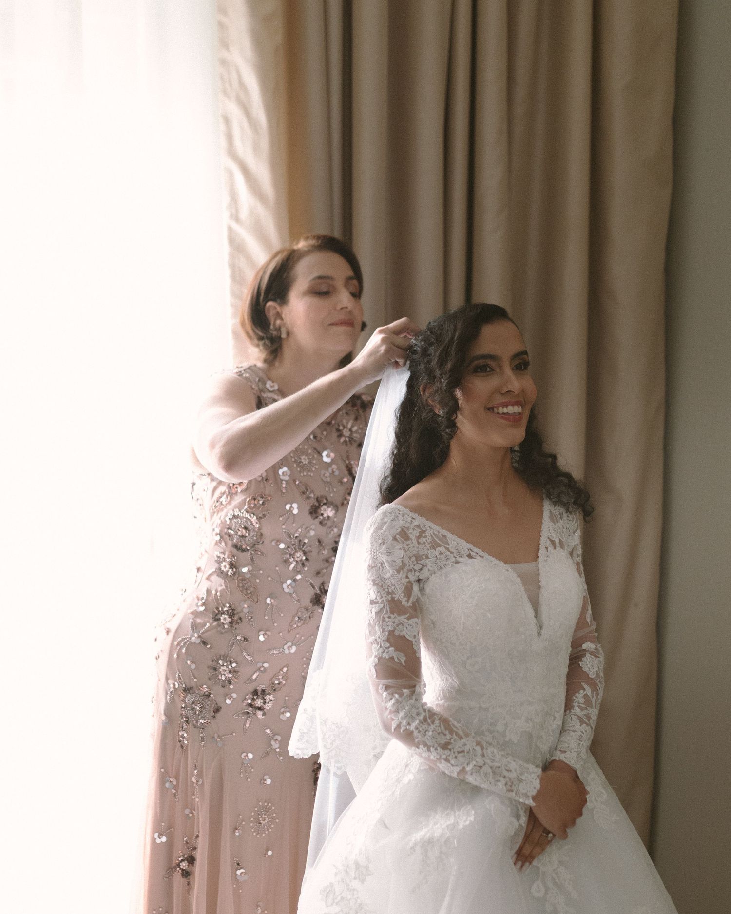 Bride in soft window light, framed through a doorway for an intimate, candid getting-ready moment.