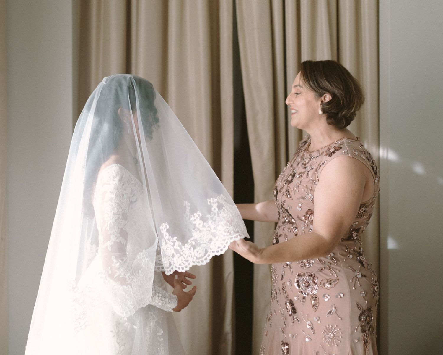 Bride in soft window light, framed through a doorway for an intimate, candid getting-ready moment.