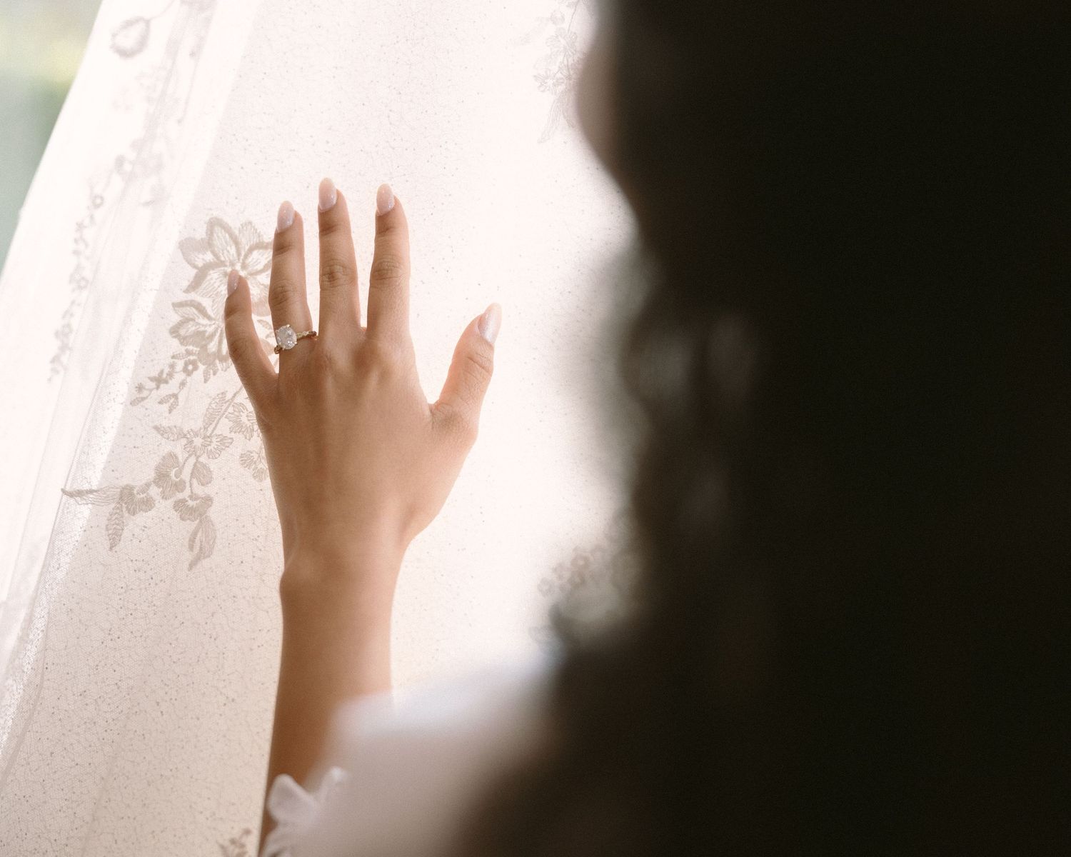 Bride in soft window light, framed through a doorway for an intimate, candid getting-ready moment.