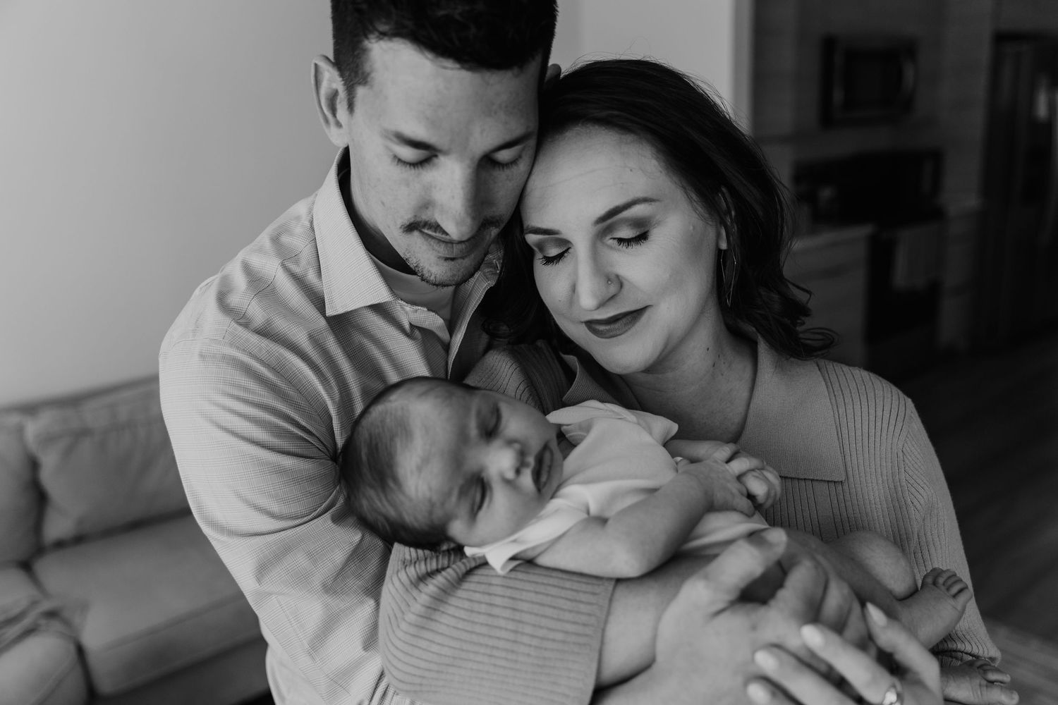 Black and white photo of new parents tenderly holding their sleeping newborn baby.