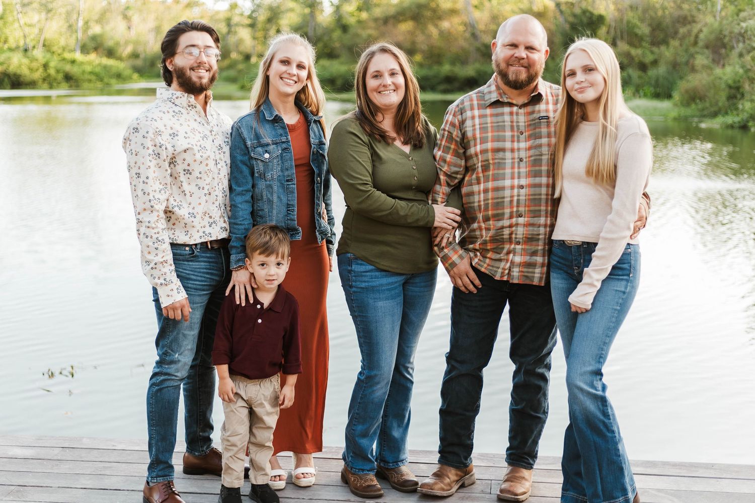 Smiling extended family of six posing together on a lakeside dock in autumn.