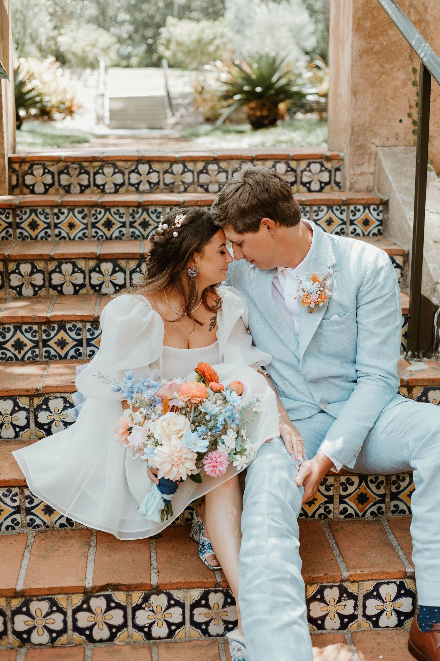 Bride and groom sitting close on decorative tiled steps, sharing an intimate moment with bouquet.