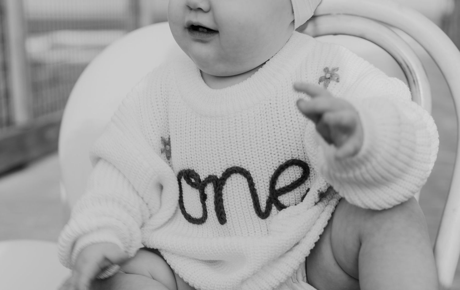 Close-up black and white photo of baby wearing a knit 'one' sweater for first birthday milestone portrait.