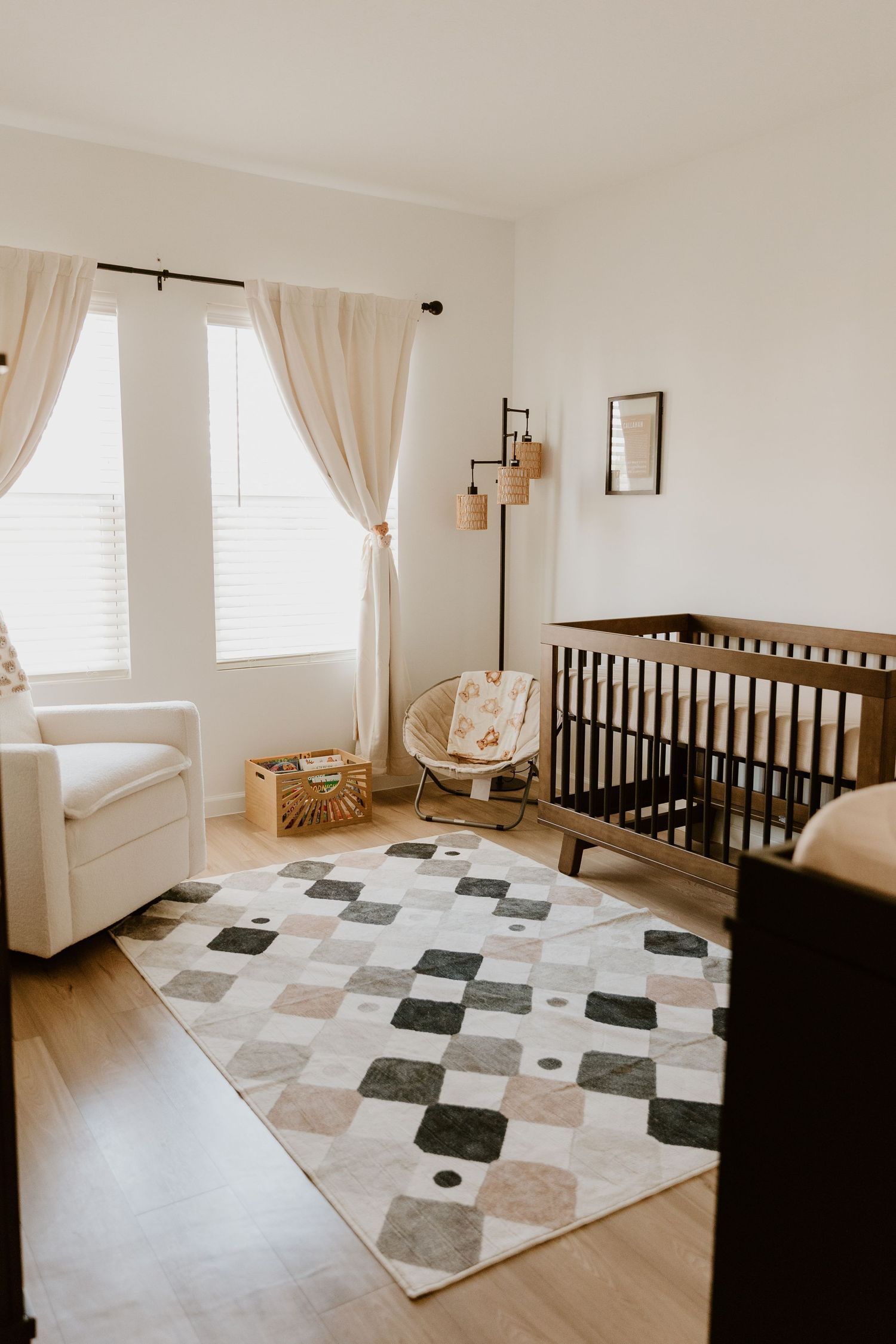 Neutral-toned nursery with dark wood crib, geometric rug, and natural light curtains.