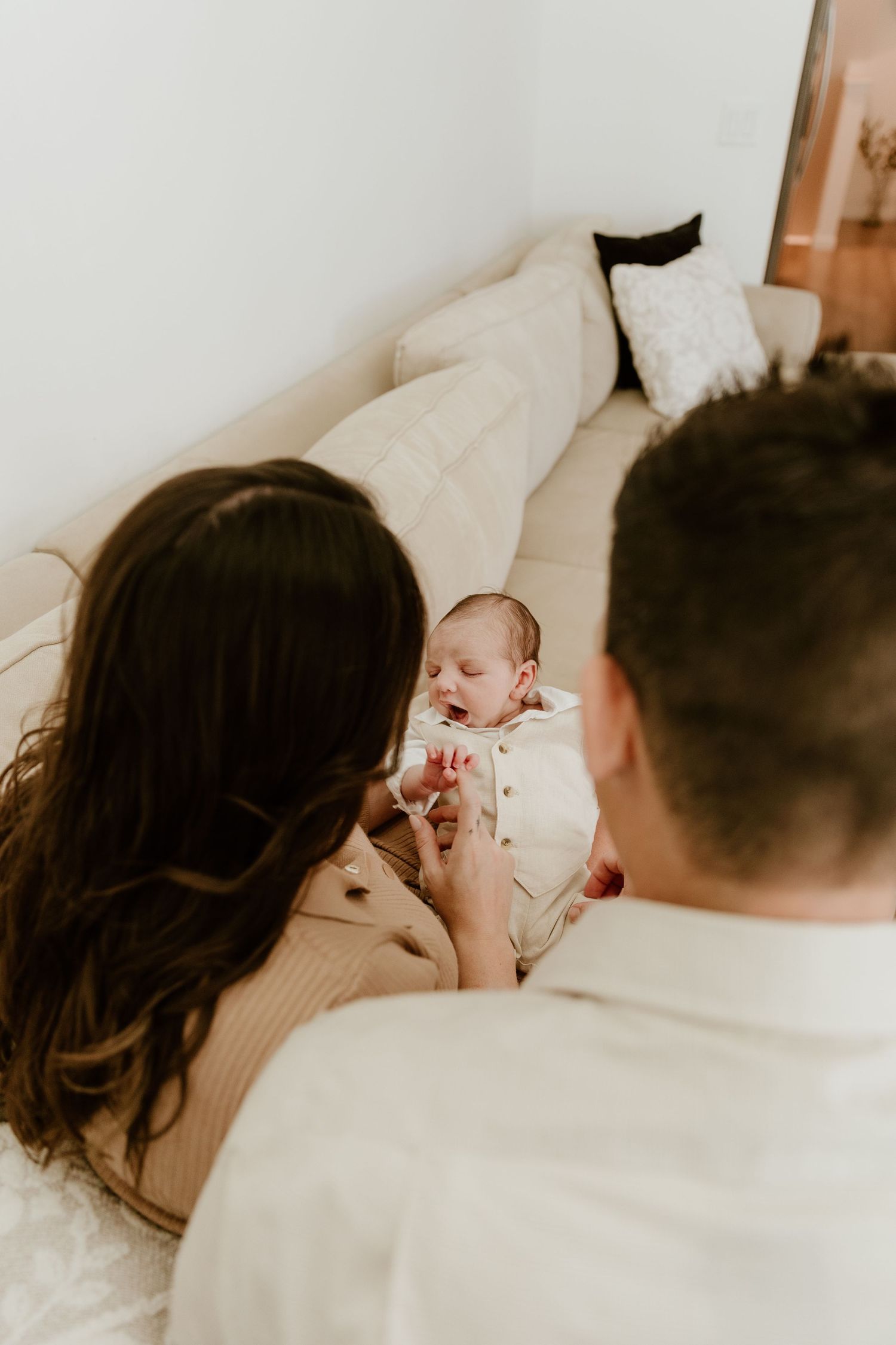 New parents gazing lovingly at their newborn baby resting on a white sofa.