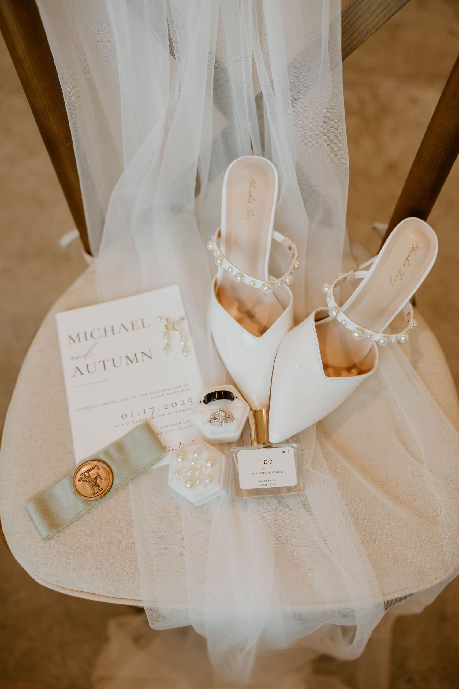 White bridal heels with pearl details on chair with veil, wedding invitation for Michael and Autumn, and accessories.