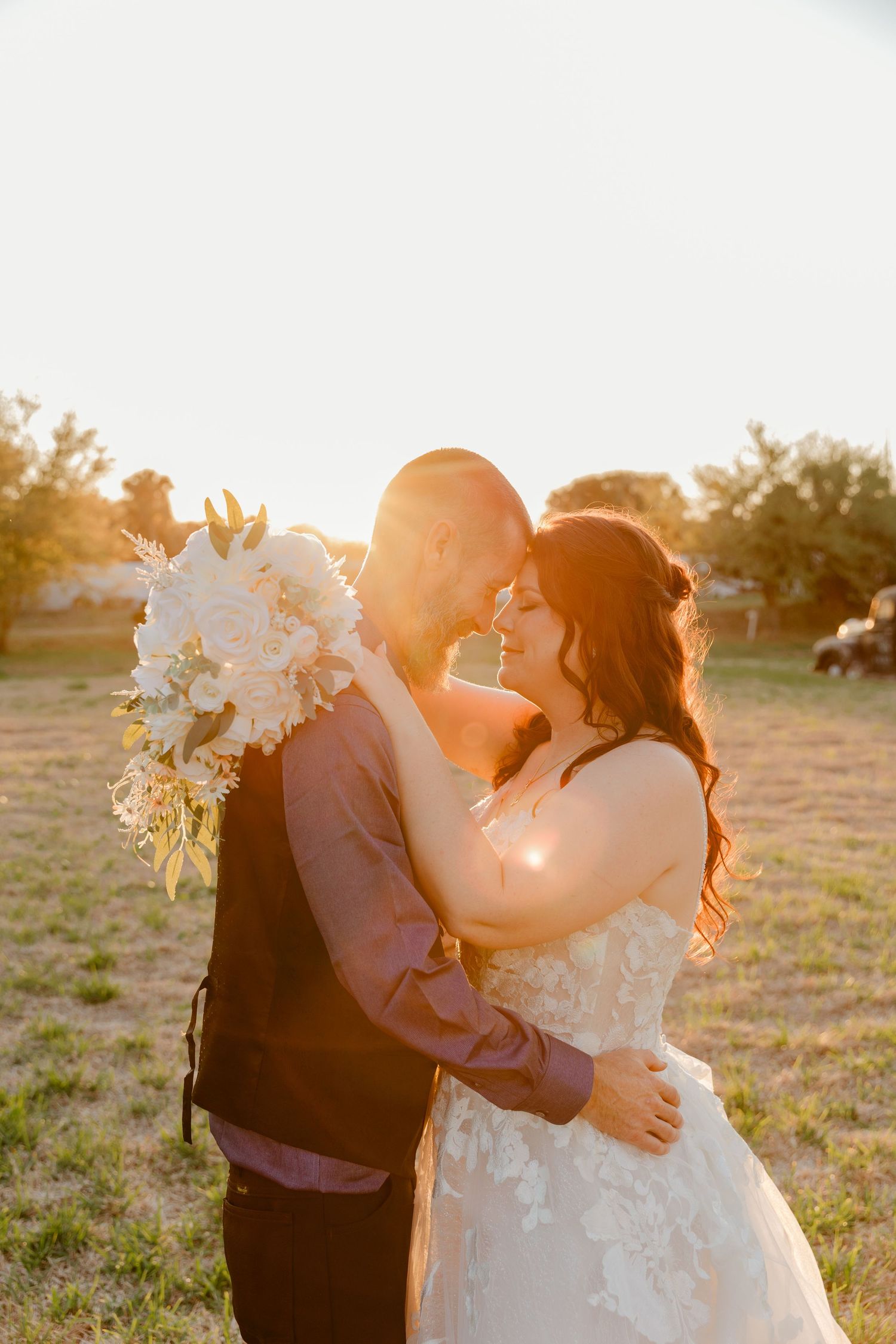 A bride and groom share a romantic golden hour moment outdoors, with the bride holding a white floral bouquet.