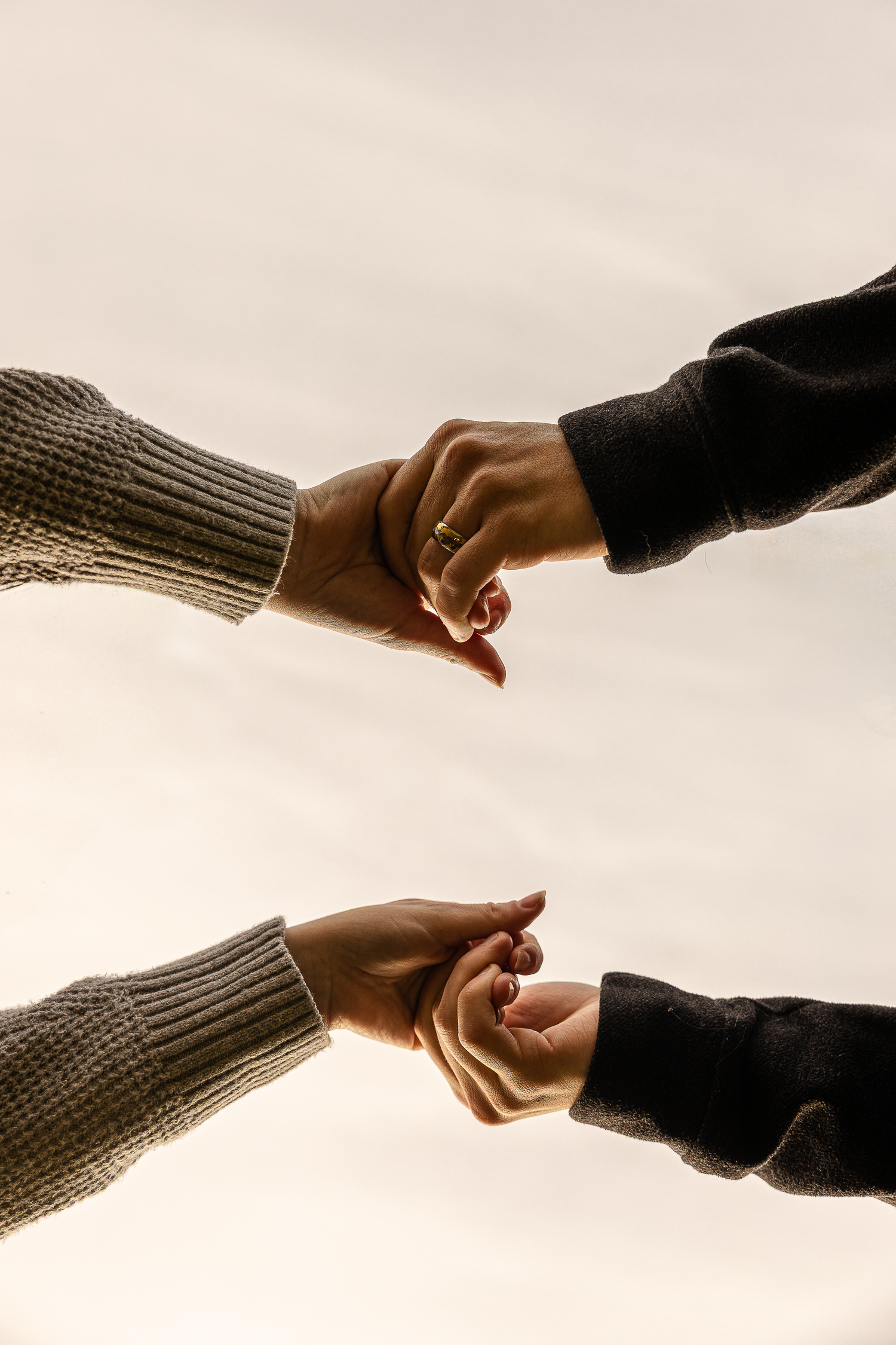 Two pairs of hands reaching towards each other against a light background while wearing knit sweater sleeves.