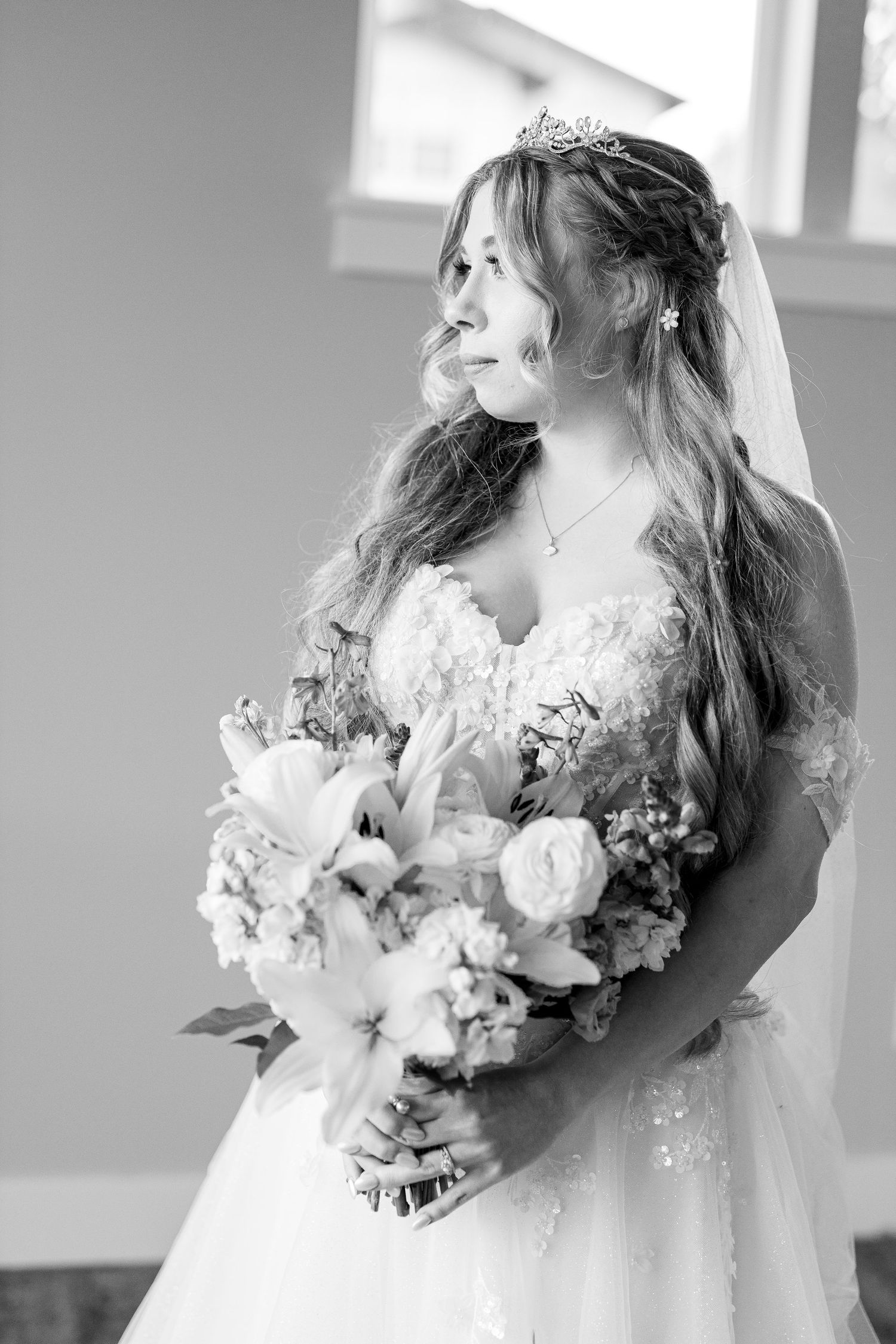 A dreamy black and white bridal portrait holds a romantic bouquet of light-colored flowers against a white gown.
