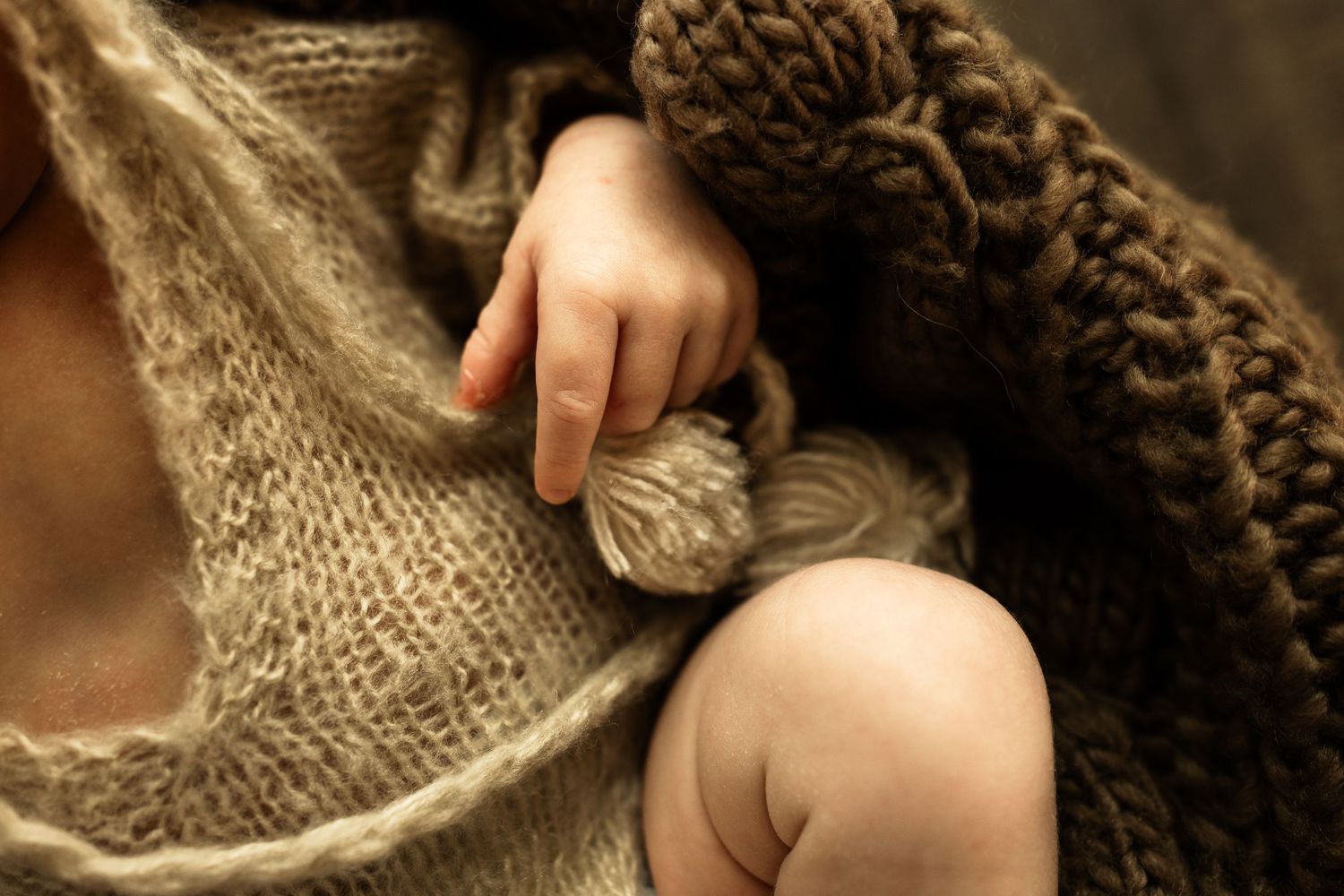 Close-up of a newborn baby's tiny hand resting on a soft knit blanket, capturing delicate infant details.