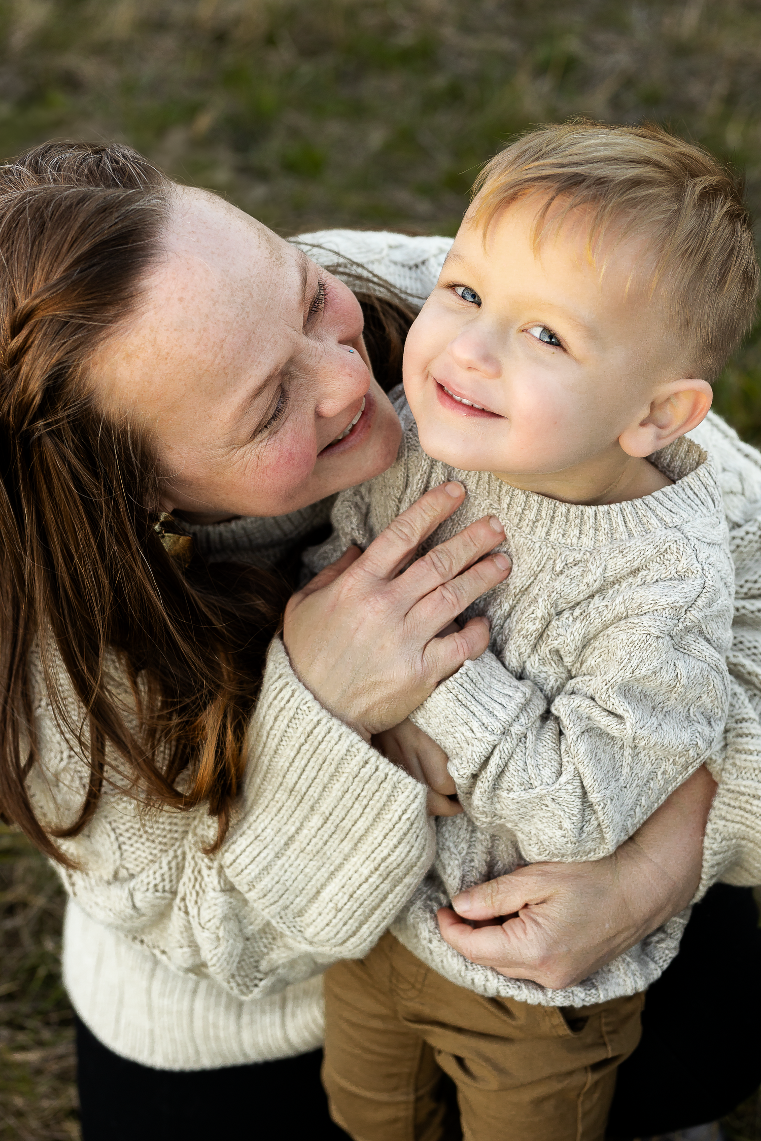 Tender moment shared between parent and child wearing matching cream sweaters in natural outdoor setting.
