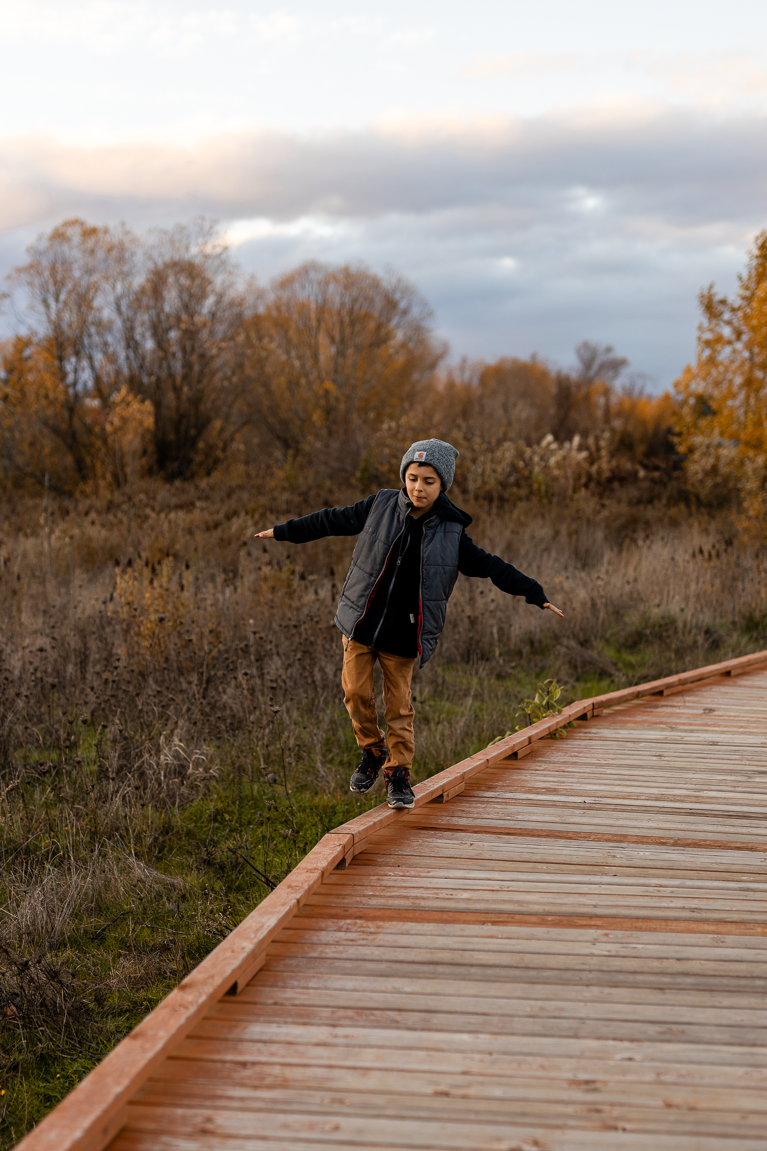 Young person balancing on wooden boardwalk during golden autumn sunset.