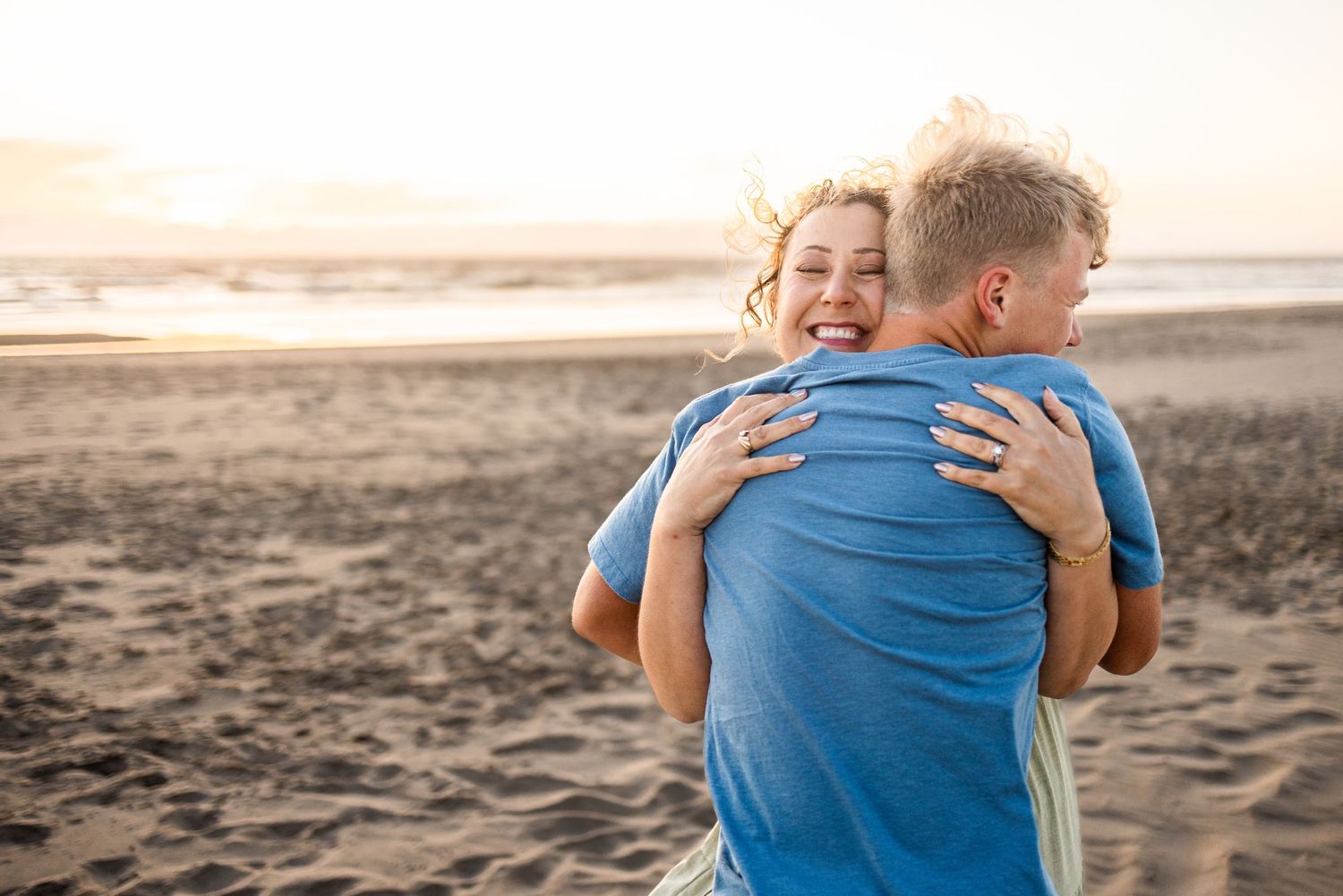 A happy couple embracing on a sandy beach at sunset, wearing blue shirts.