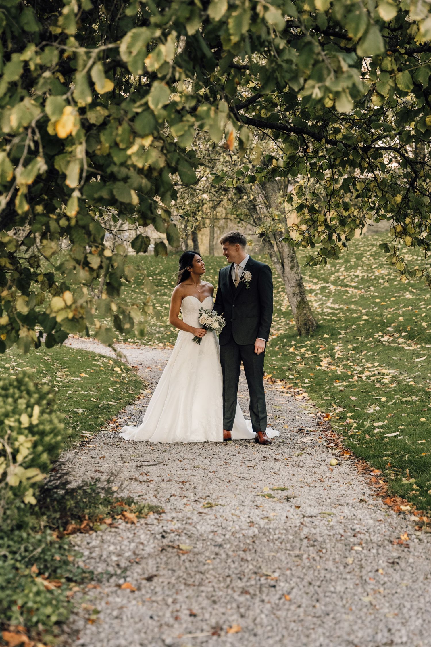 Couple walking along a gravel path surrounded by autumn foliage and falling leaves.