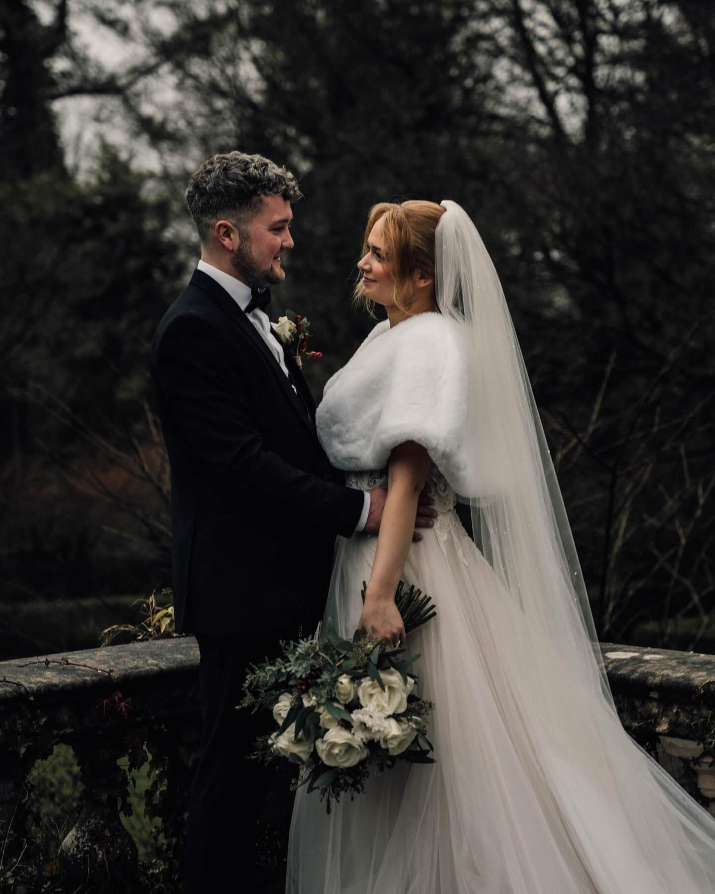 Romantic wedding couple embracing outdoors in a moody dark setting with white bouquet.