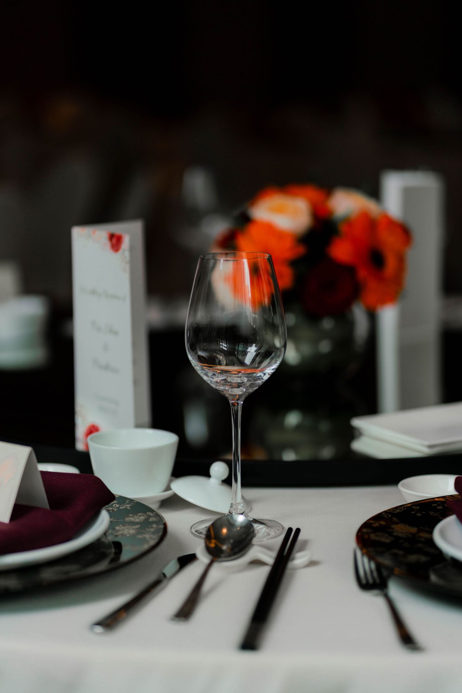 An elegant table setting with wine glasses, purple napkins, and orange floral accents creates a romantic dining atmosphere.