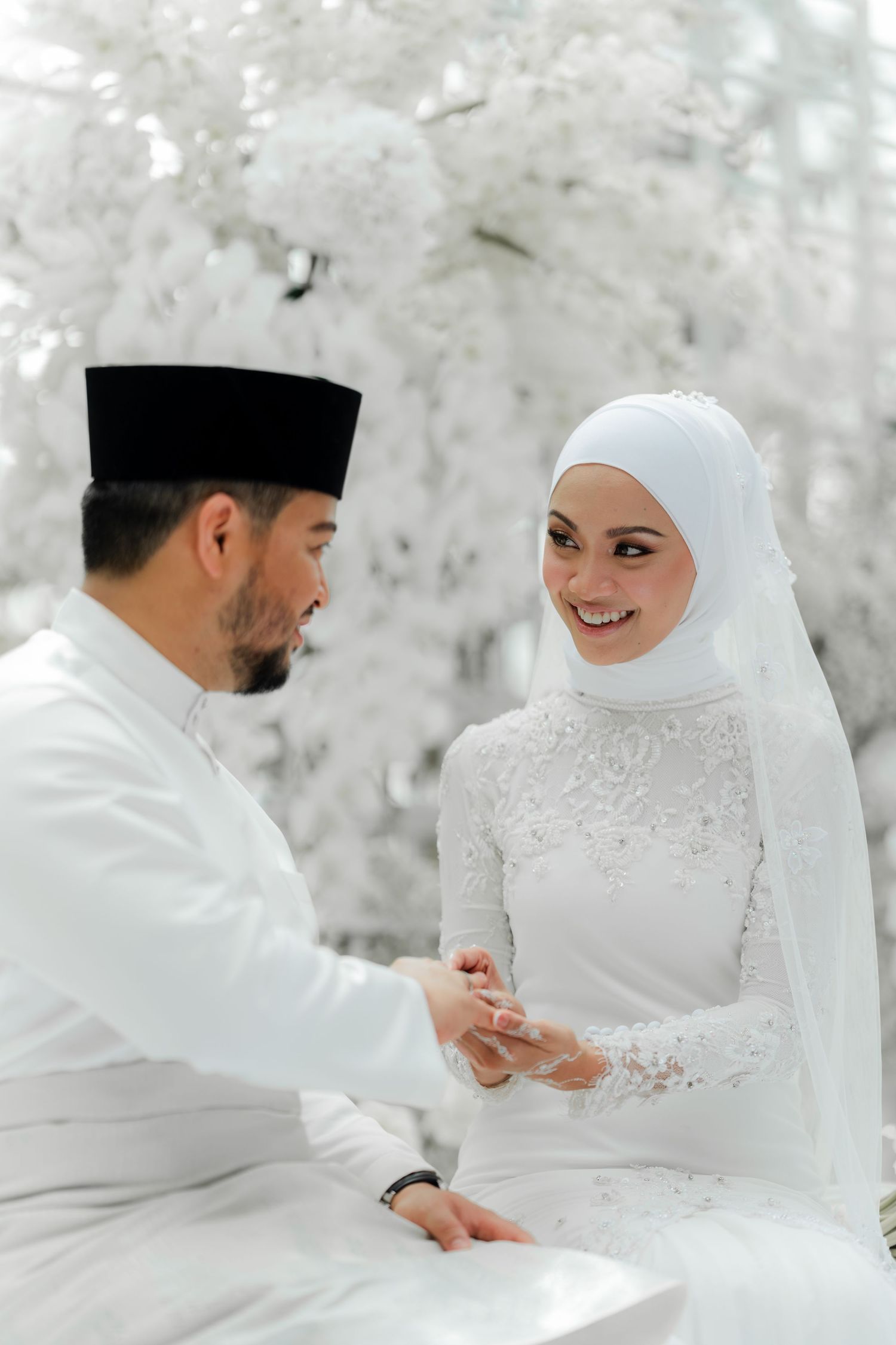 A Muslim couple in traditional white attire exchange rings during their wedding ceremony.