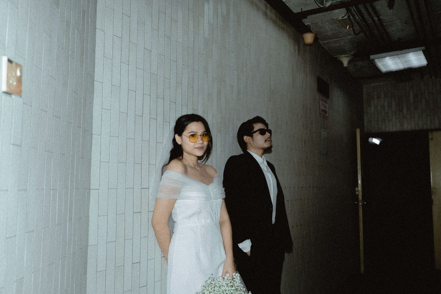 A couple stands in a minimalist hallway wearing formal attire during their wedding.