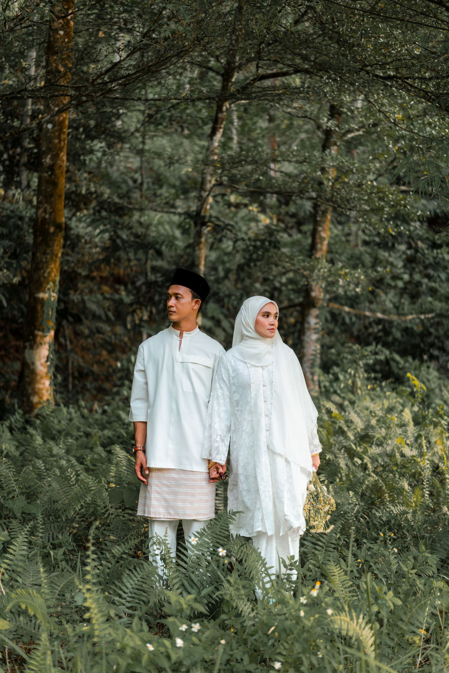 Muslim couple in white traditional attire holding hands in a lush green forest setting.