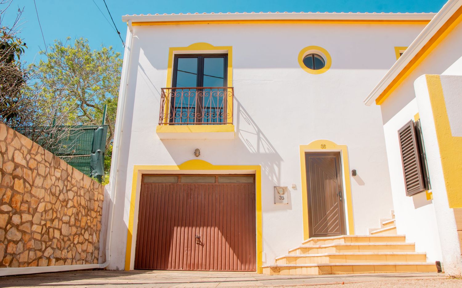 Modern white Mediterranean villa with brown garage door and steps leading to front entrance in warm sunlight.