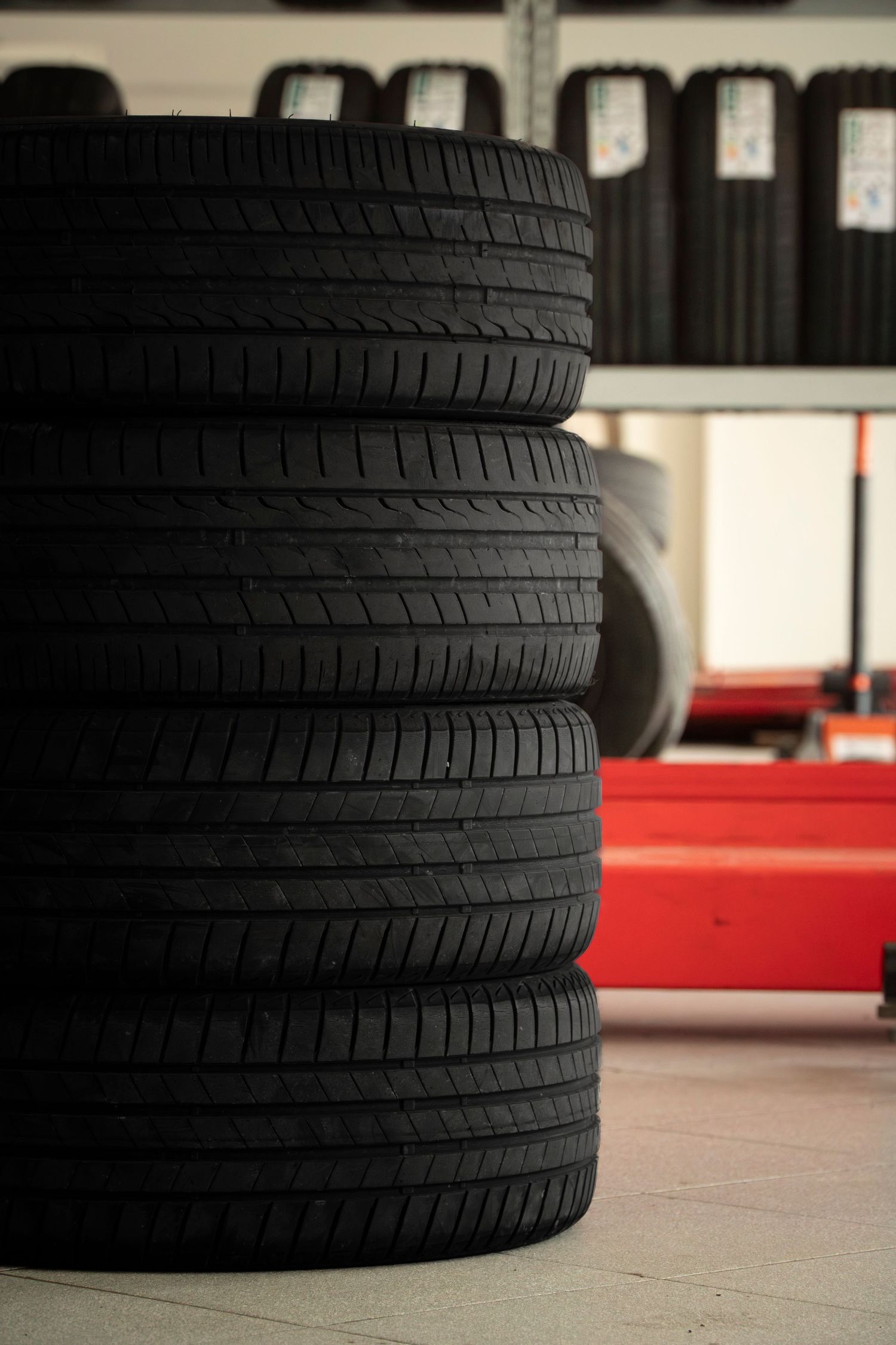Stack of four black car tires in an auto shop with more tires on shelves in the background.