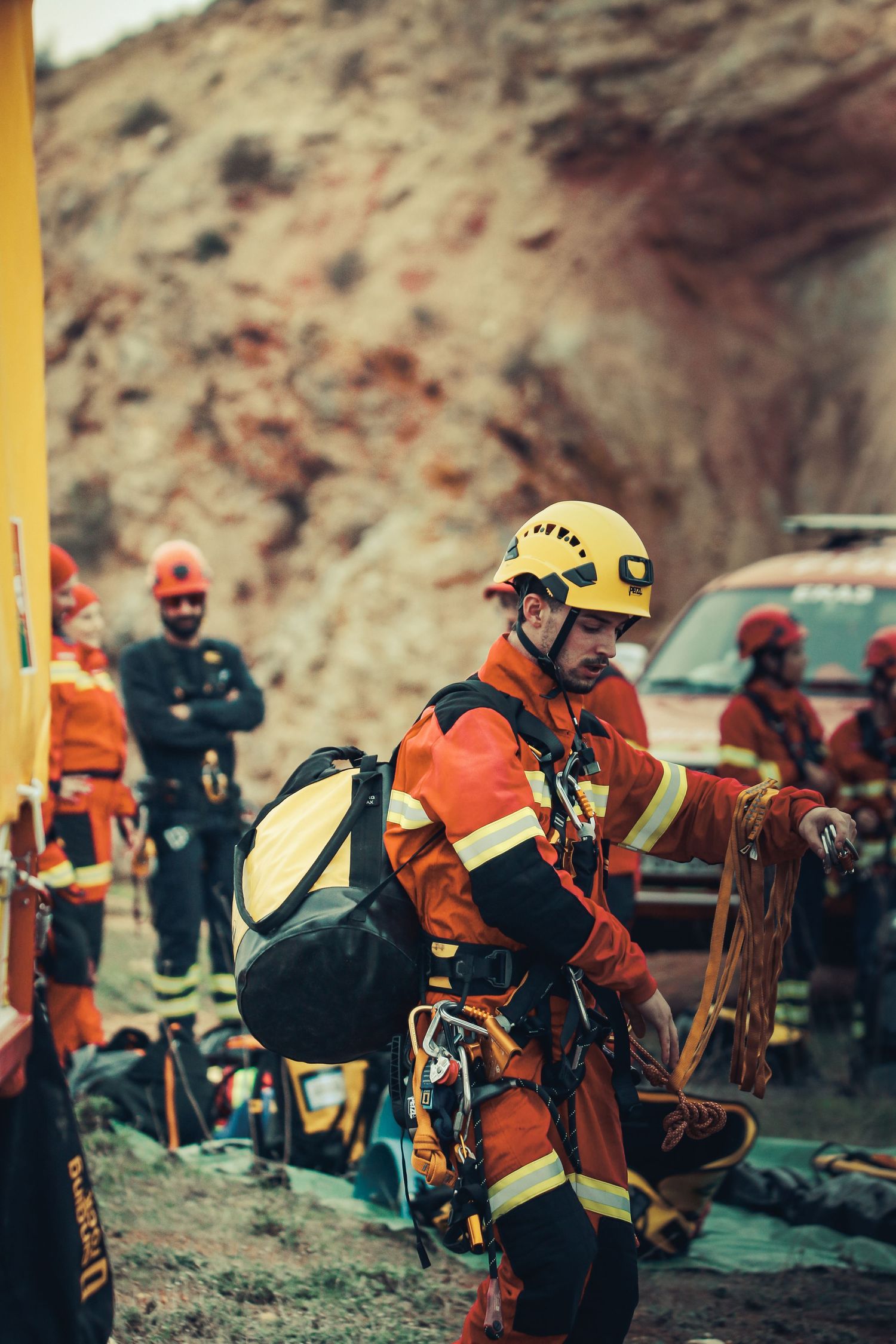 Rescue worker in orange safety gear and yellow helmet with climbing equipment preparing for mountain operation.