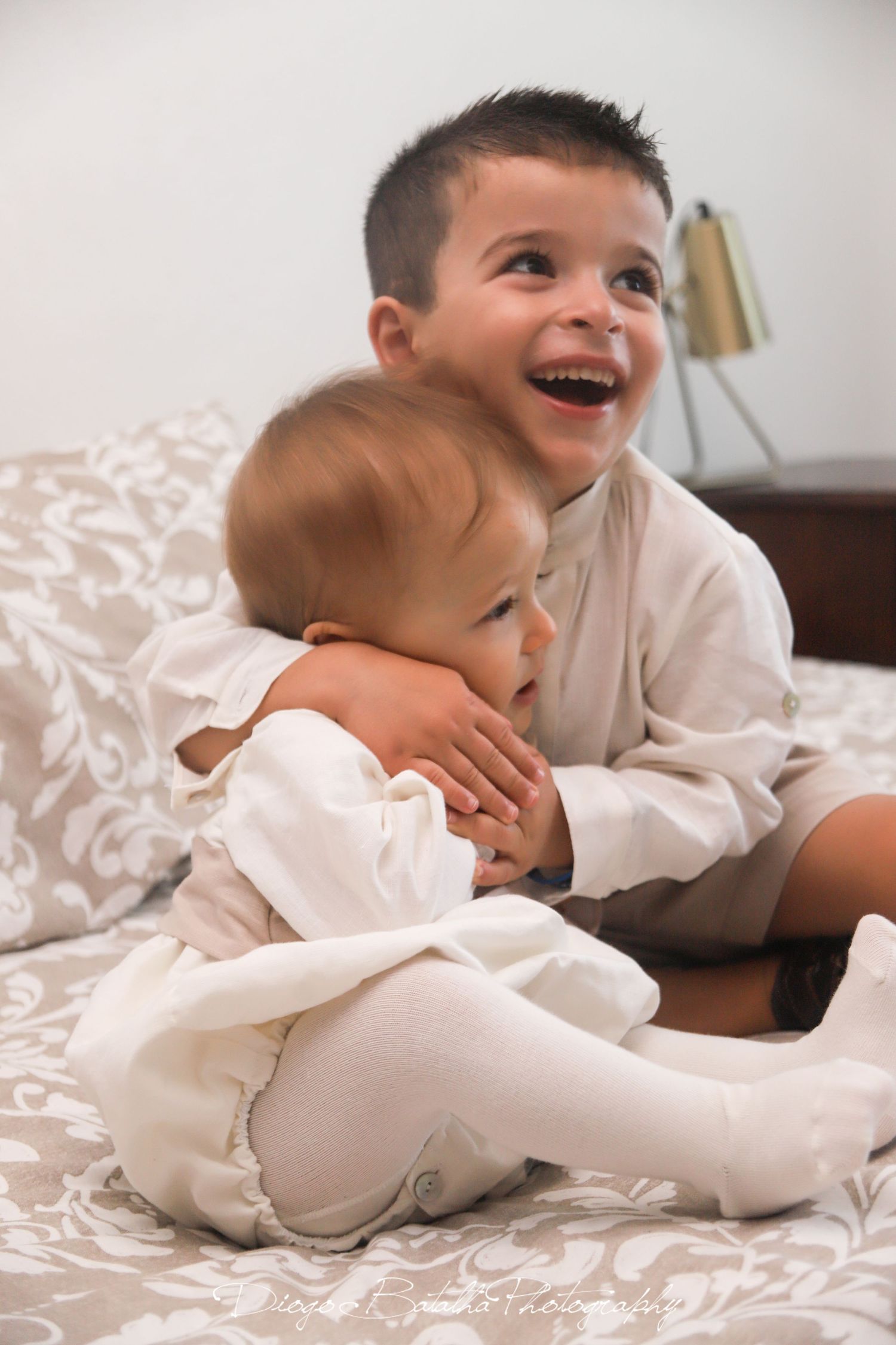 Children in white clothing sharing playful moments on a bed.