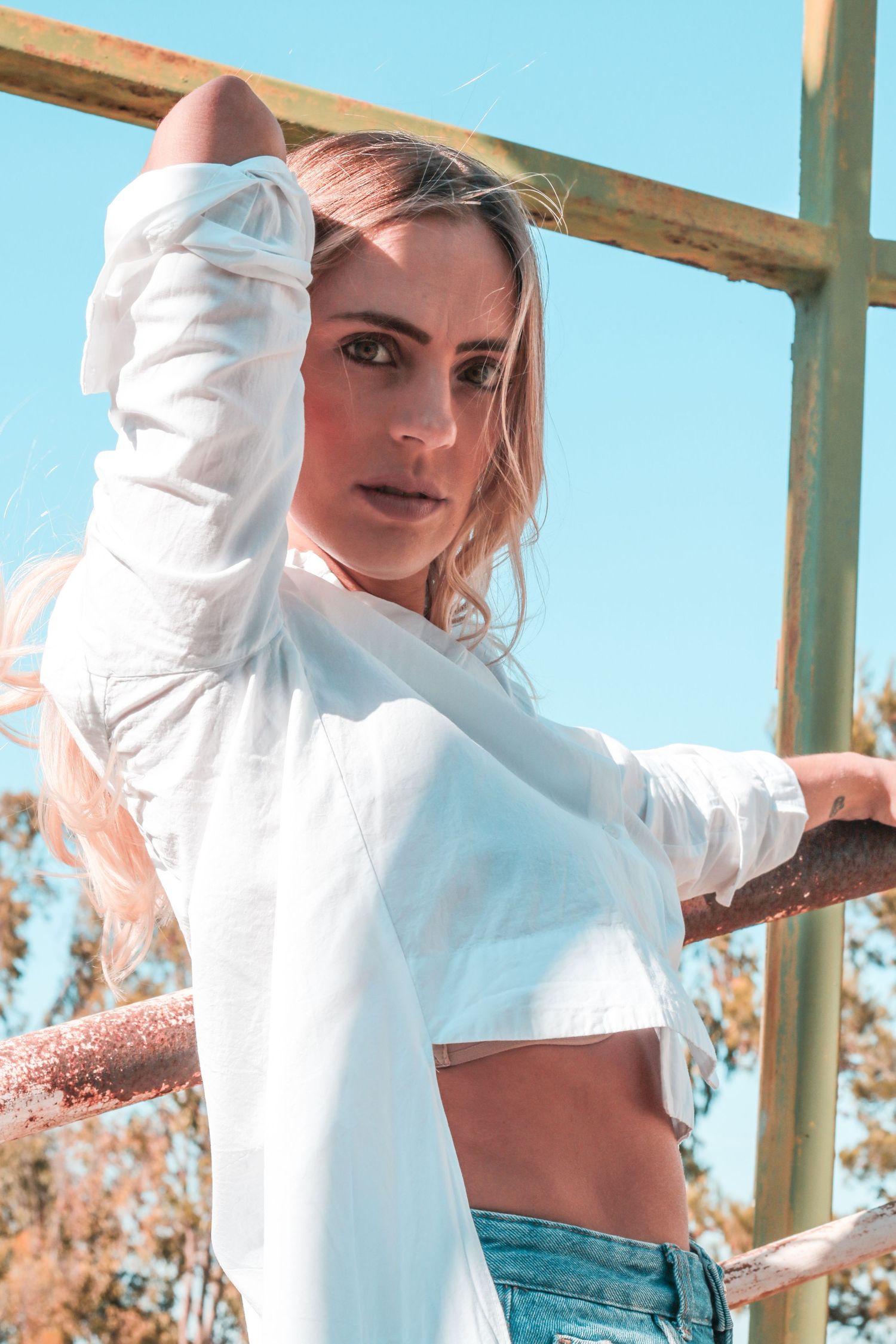 Person in cropped white sweater and jeans poses against blue sky.