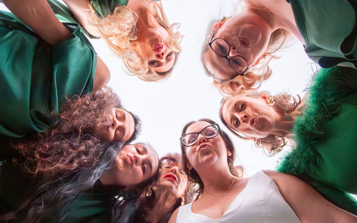 Group forming a circle looking down at camera with joyful expressions.
