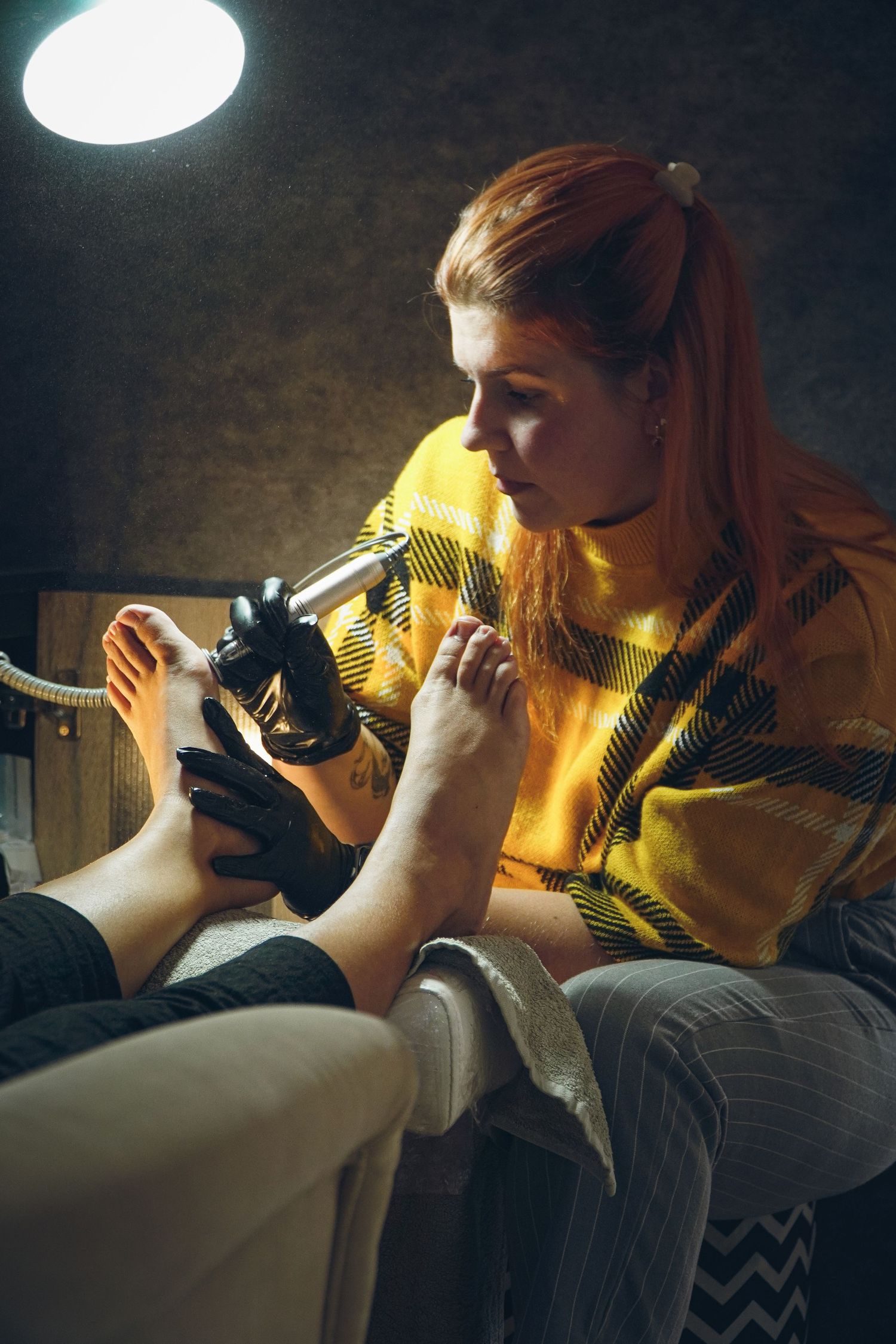 Professional performing pedicure service while wearing protective gloves in warm lighting.