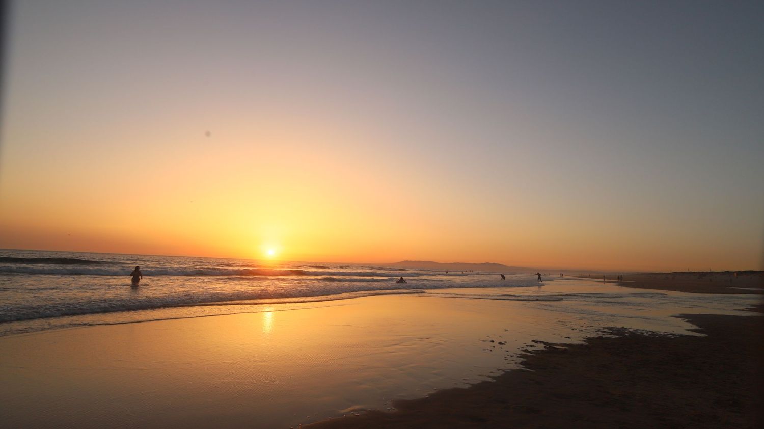 Beautiful sunset over a beach with silhouetted figures in the distance and reflective water on the sand.