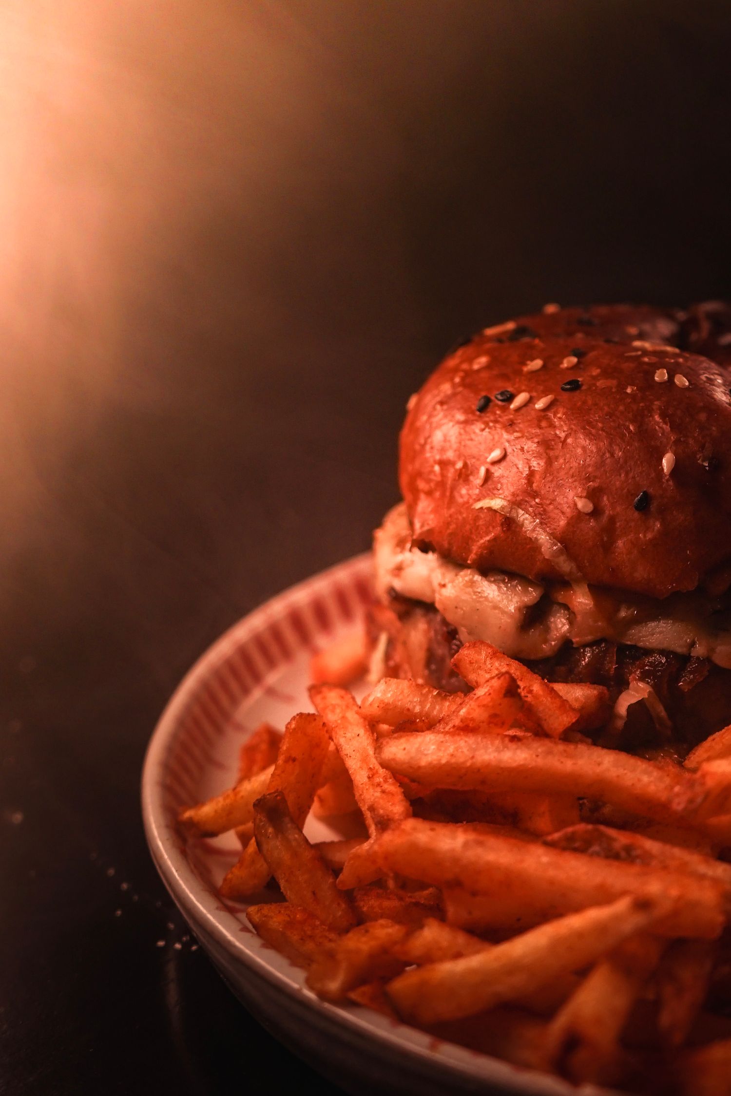 Burger and french fries on a plate illuminated with dramatic lighting.