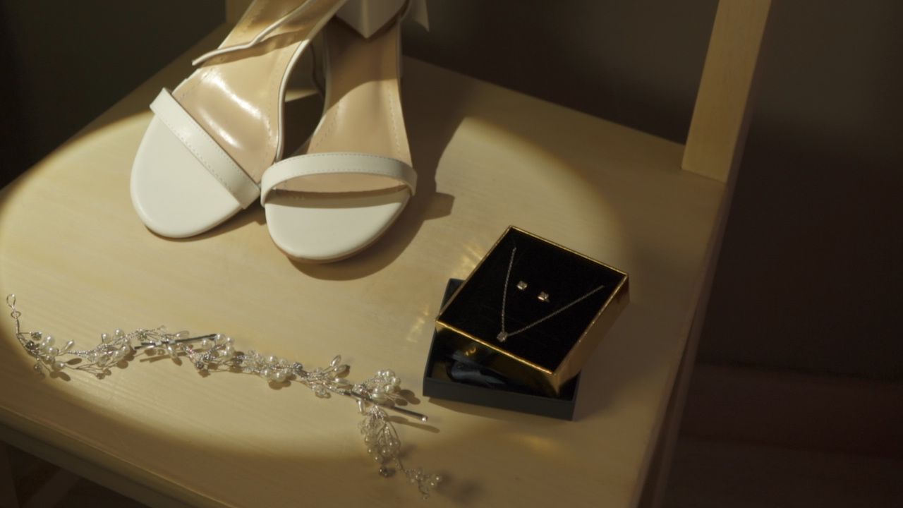 Wedding accessories including white shoes and jewelry box arranged in dramatic lighting.
