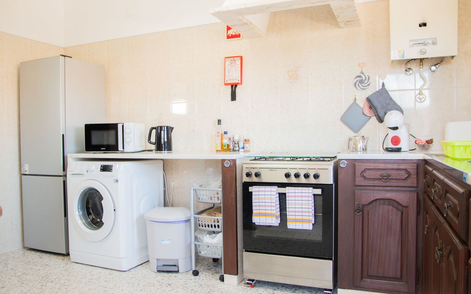 Modern kitchen interior with white appliances including refrigerator, washing machine, microwave and gas stove.