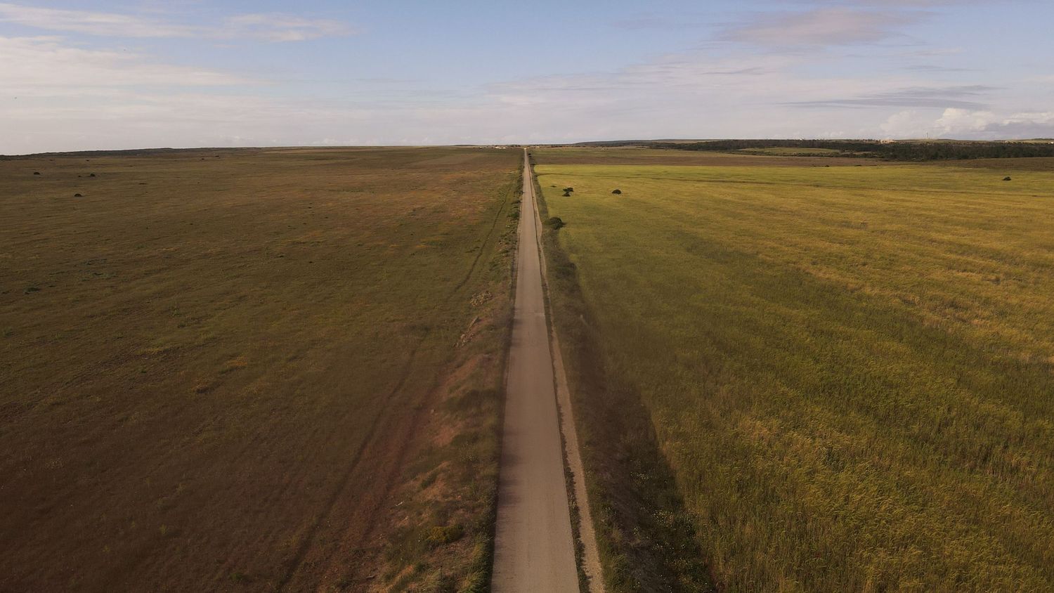 A long pipeline stretches across an empty landscape of rolling hills and grasslands at sunset.