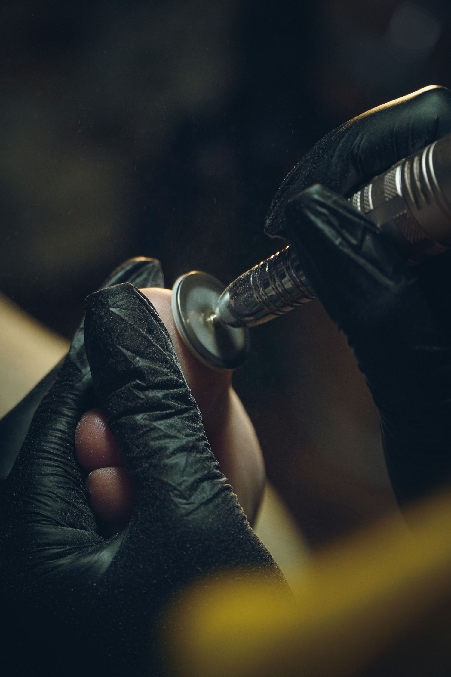 Close-up shot of hands in black gloves using a rotary tool on a metallic surface in a dimly lit workspace.