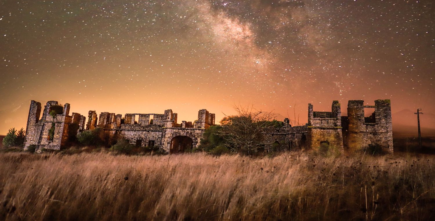 Abandoned stone castle ruins stand under a starlit sky with the Milky Way galaxy visible in the golden-hued night.