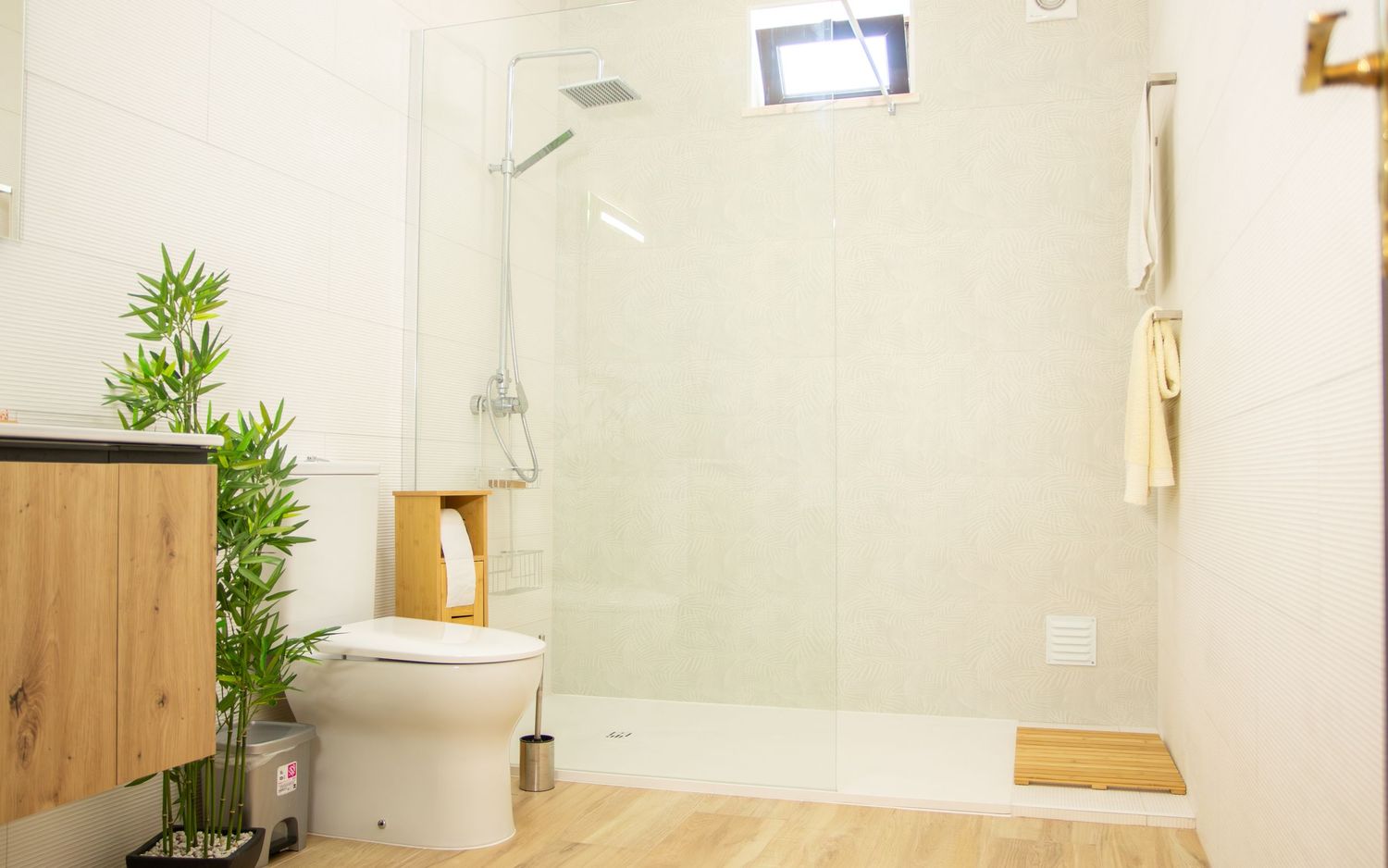 Modern minimalist bathroom interior with glass shower, wooden accents, and potted bamboo plant for natural decor.