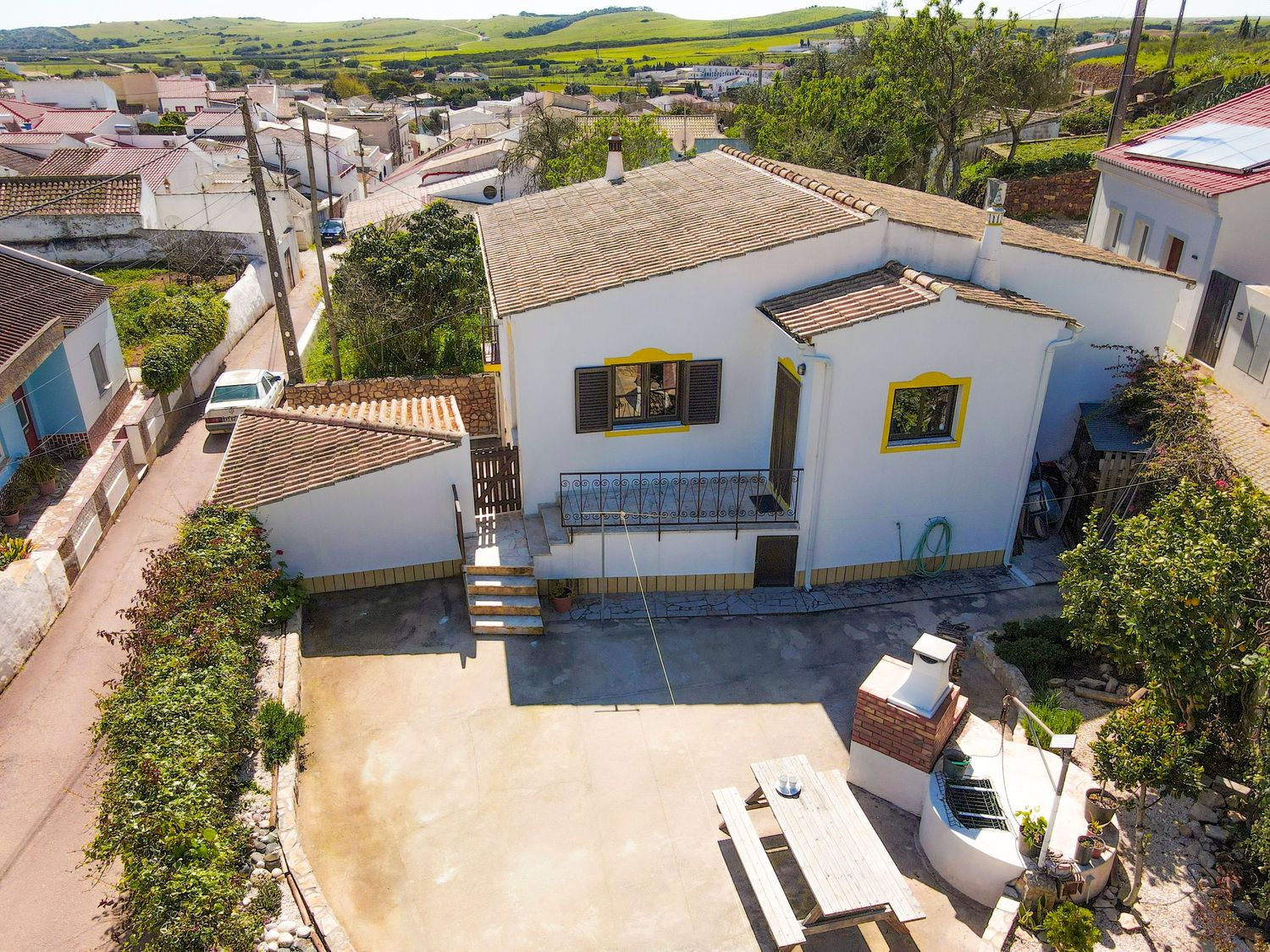 Aerial view of modern white house with two yellow windows and paved driveway in a residential area surrounded by greenery.