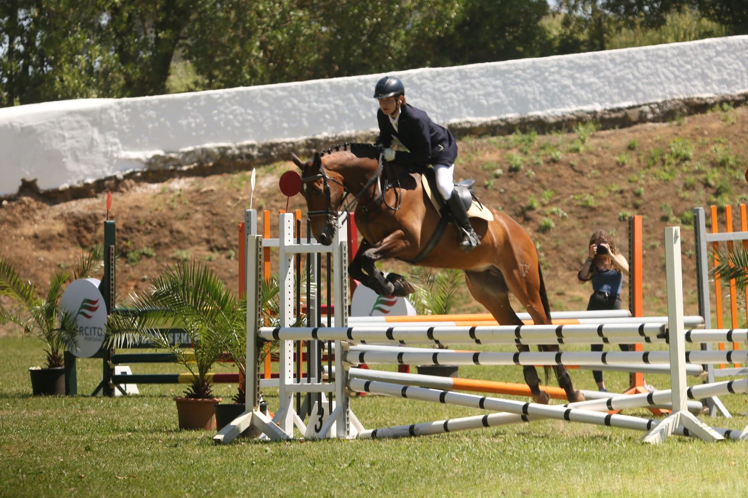Equestrian rider and horse clearing multiple white and yellow show jumping rails during outdoor competition event.