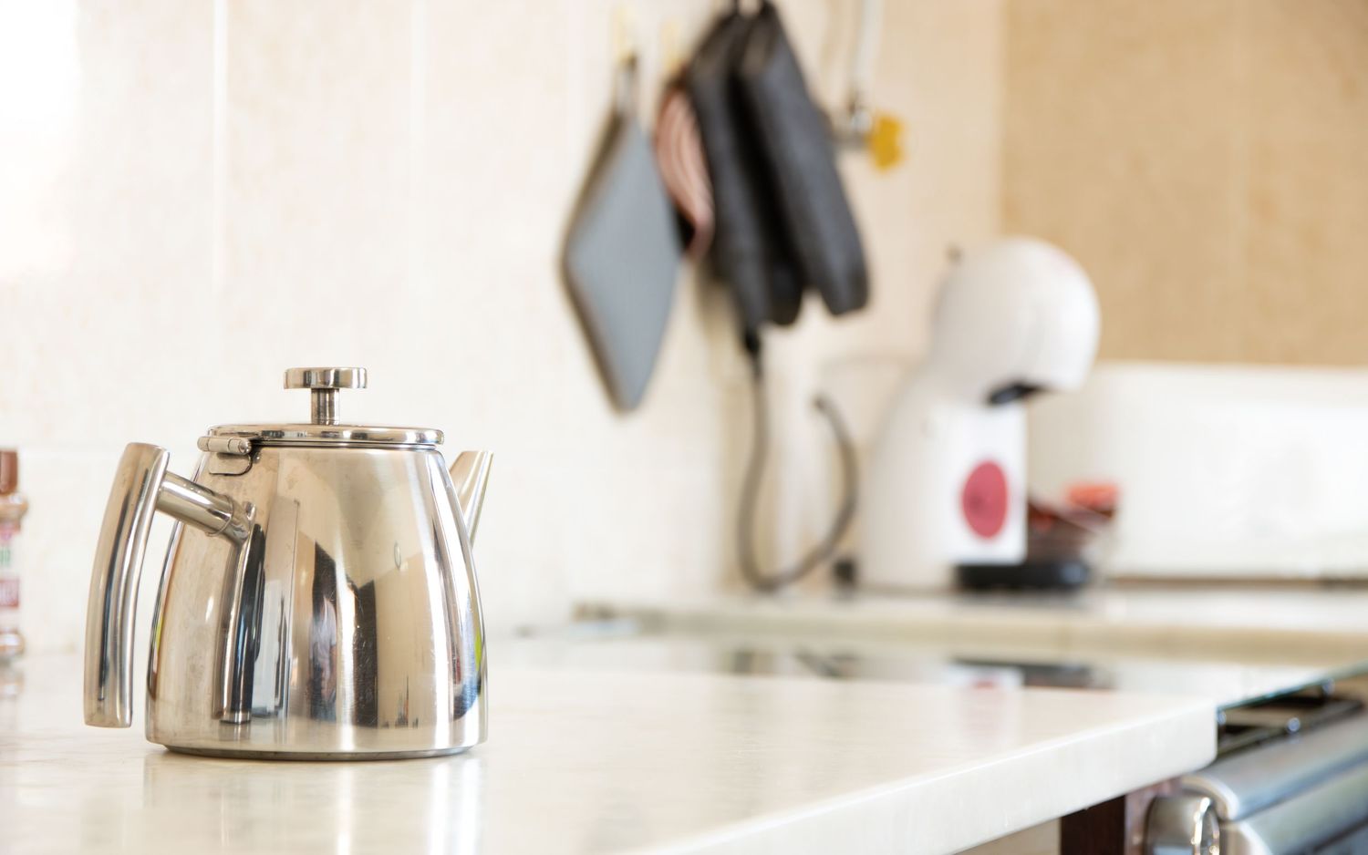 Shiny stainless steel teapot sitting on a white countertop in a modern kitchen setting.