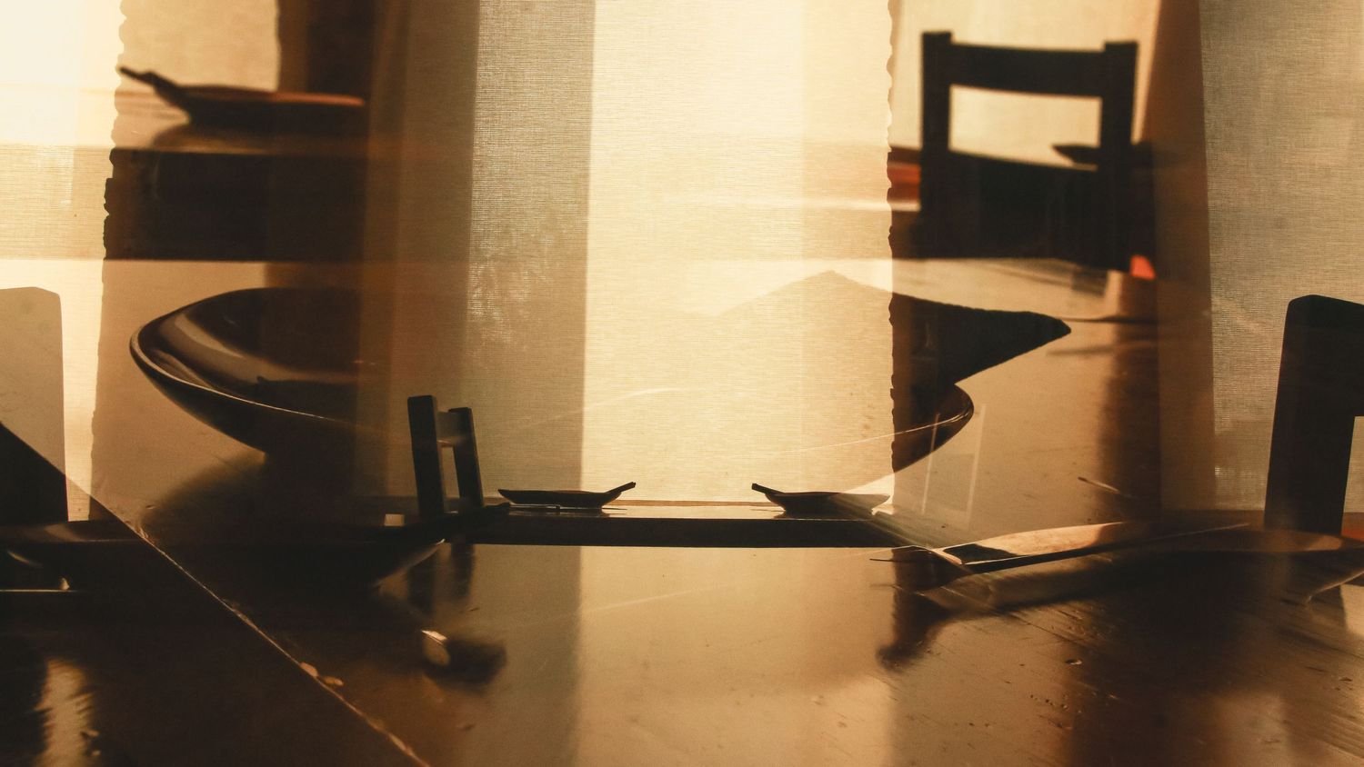 Elegant dining table setting with dark wooden chairs in moody lighting.