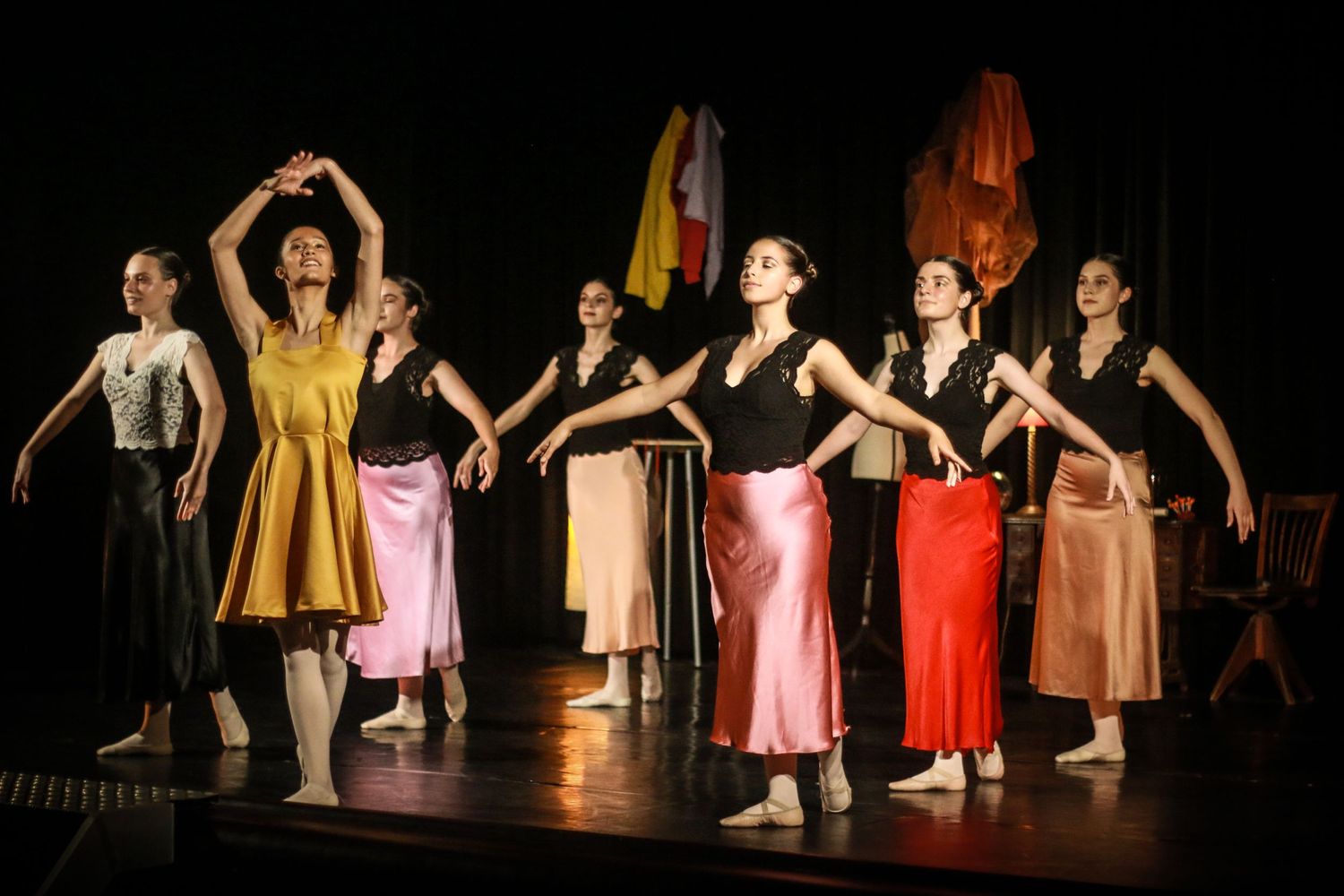 Dancers perform on stage wearing colorful vintage-style dresses in a theatrical production.