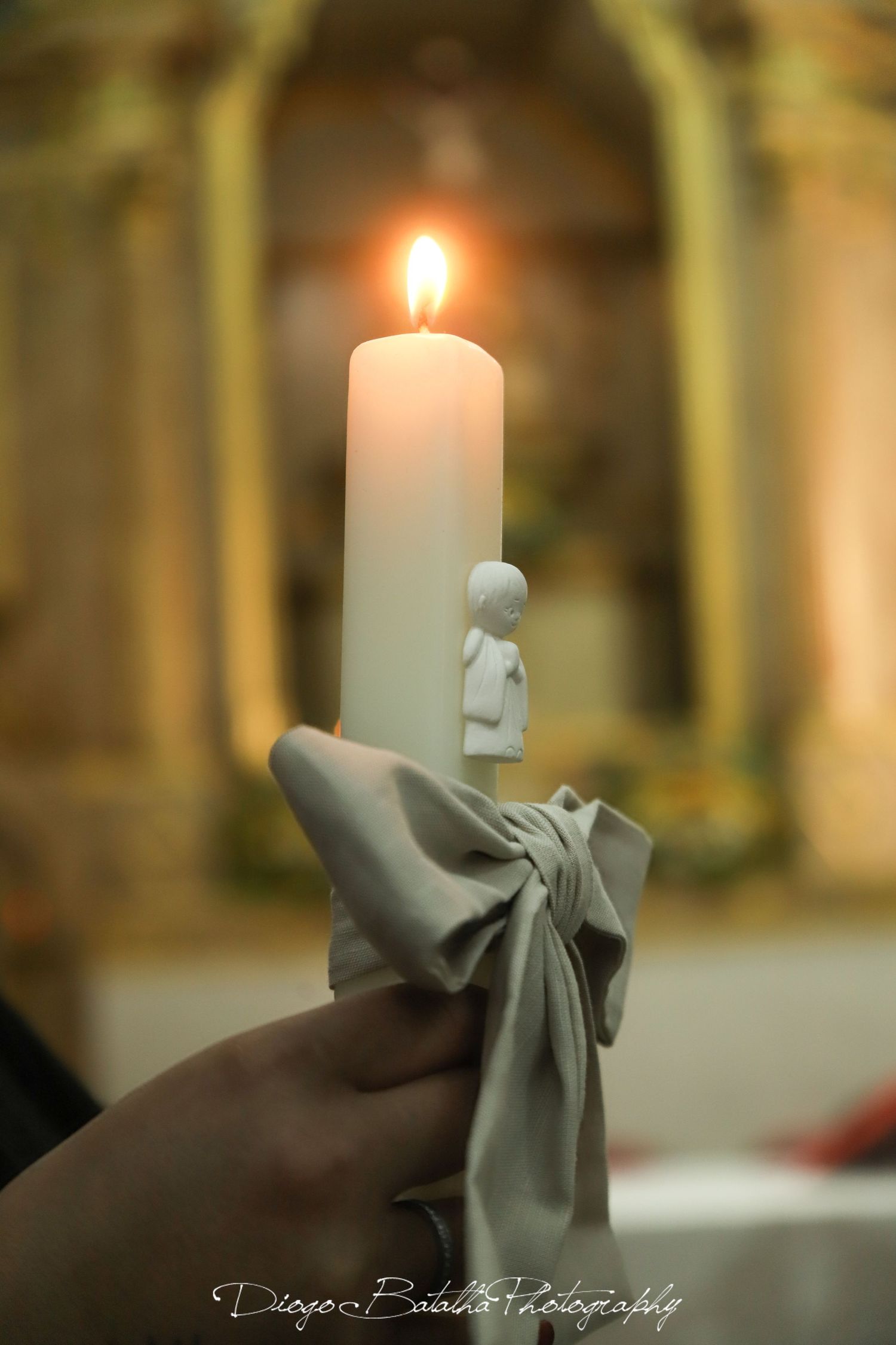 Lit white candle with decorative gray bow against blurred church background.