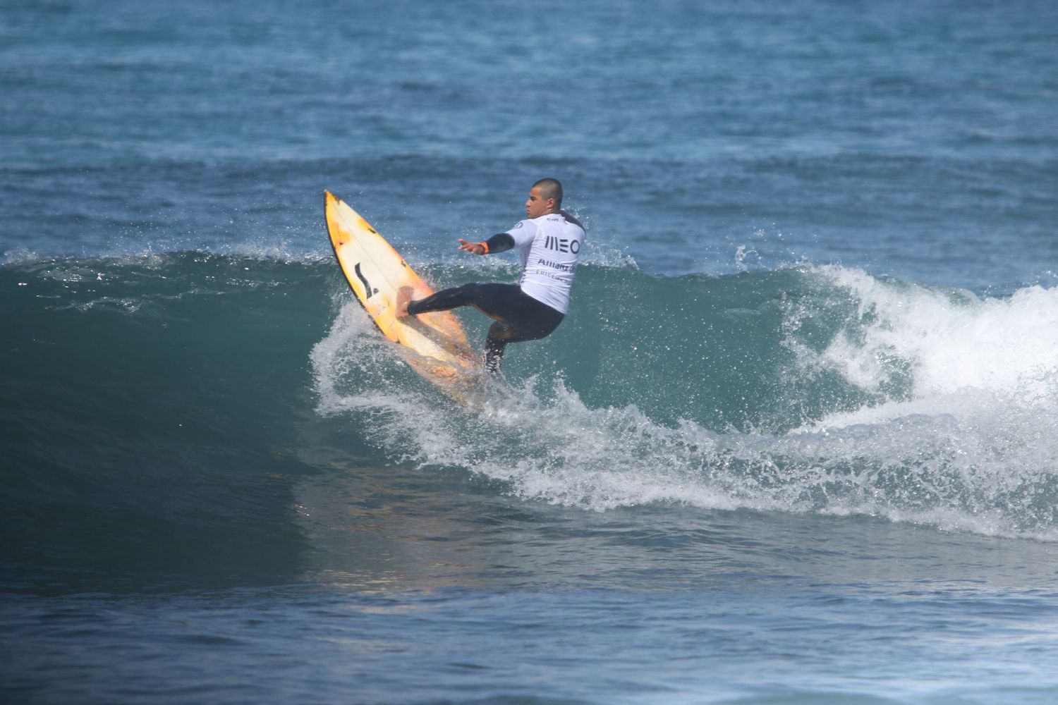 A surfer performs a smooth turn on a yellow surfboard while riding a turquoise ocean wave.