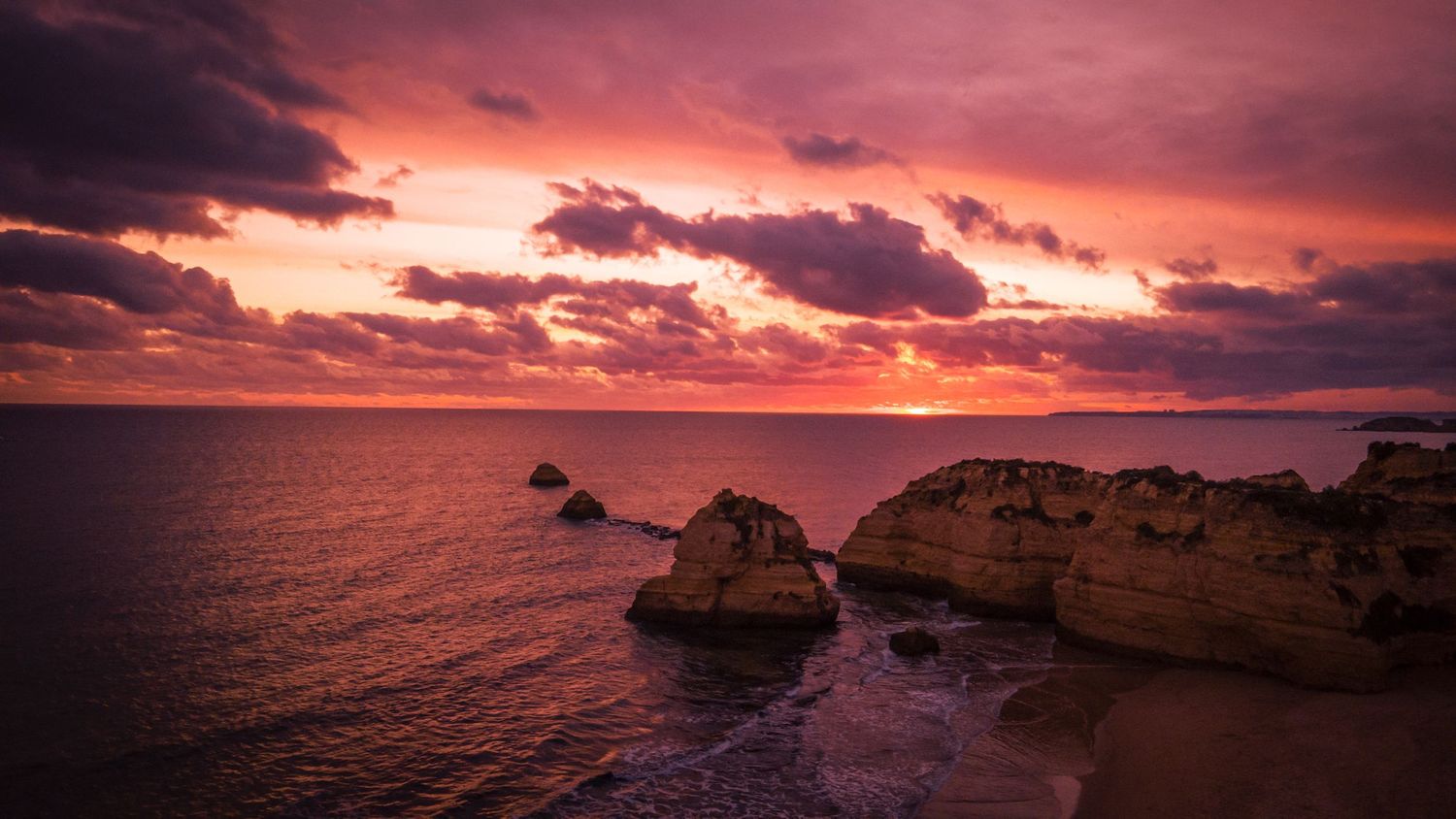 Dramatic sunset sky illuminates coastal rock formations and ocean waves along rugged limestone cliffs at dusk.