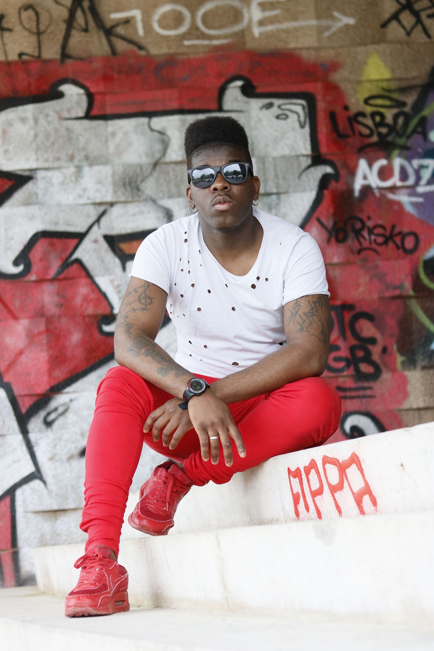 Casual urban fashion photo against graffiti wall featuring white t-shirt, red pants and matching red sneakers.