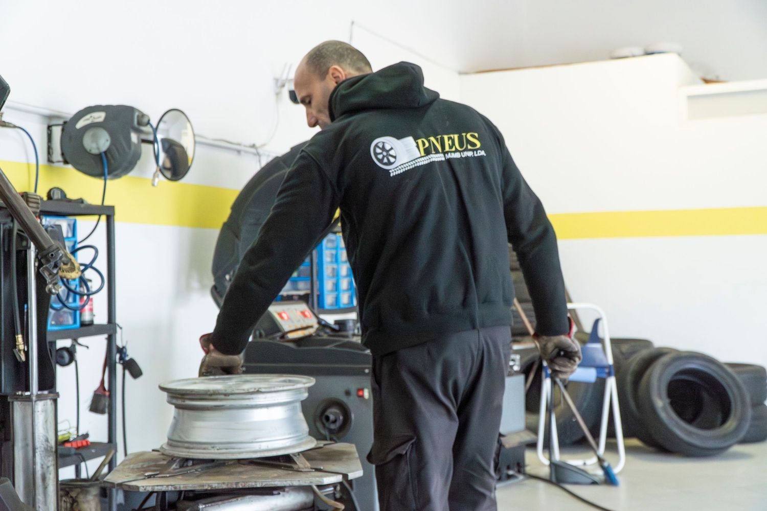 A mechanic in a Pneus jacket works on a tire rim using a tire changing machine in an auto repair shop.
