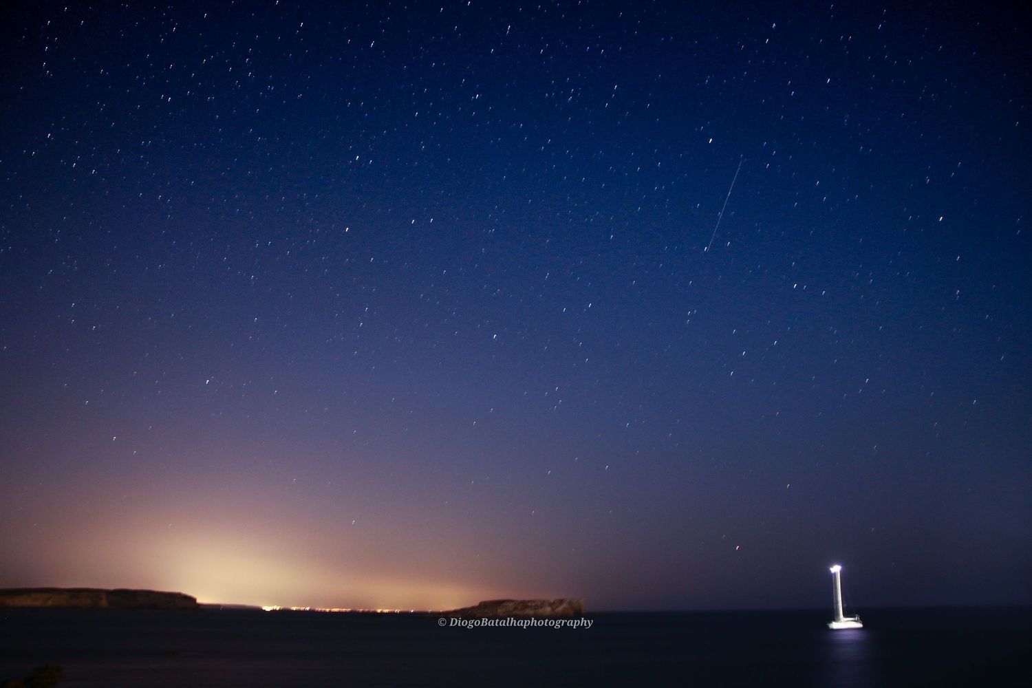 Deep blue night sky with stars over a coastal horizon.