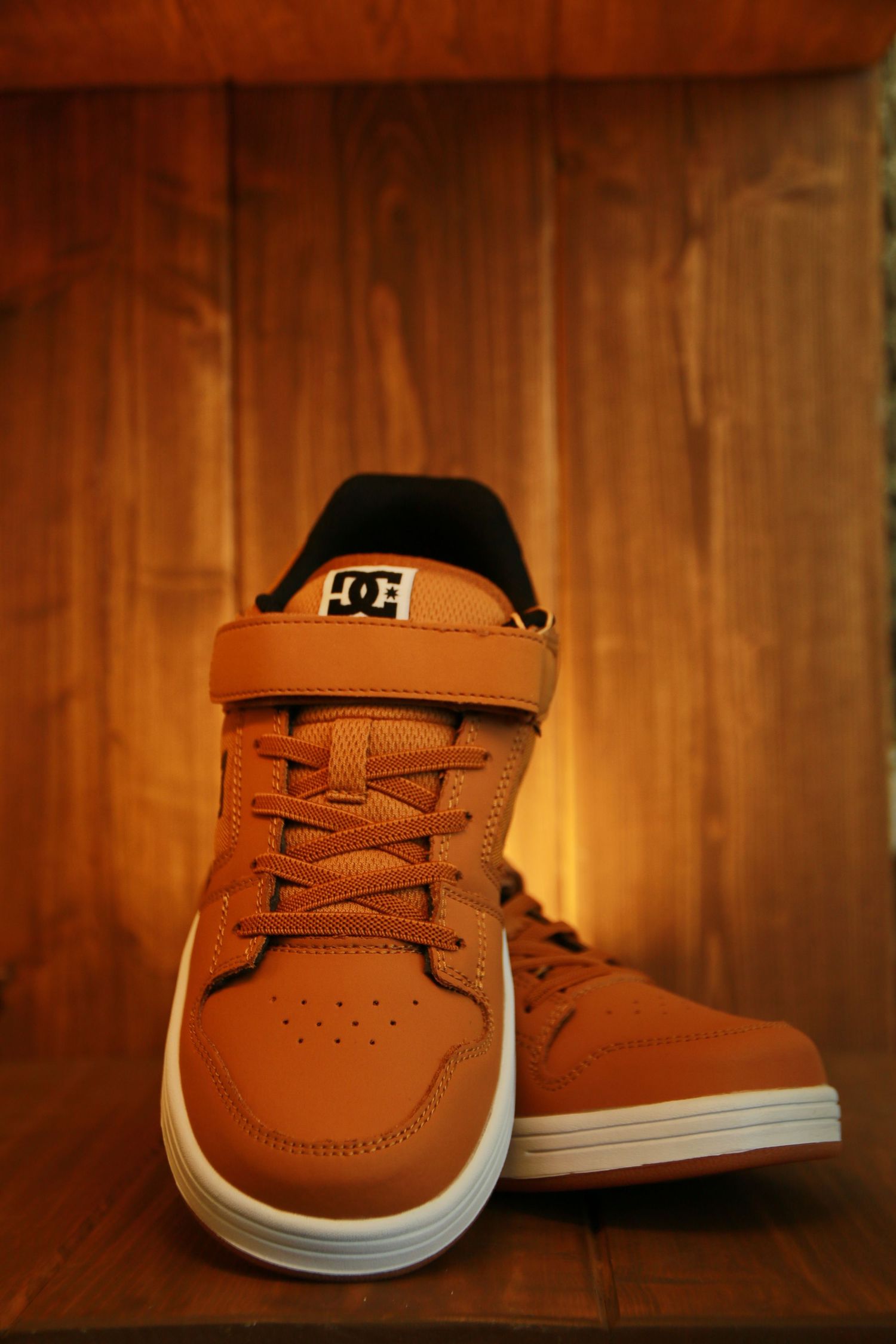 Brown leather sneakers photographed on wooden surface in warm lighting.